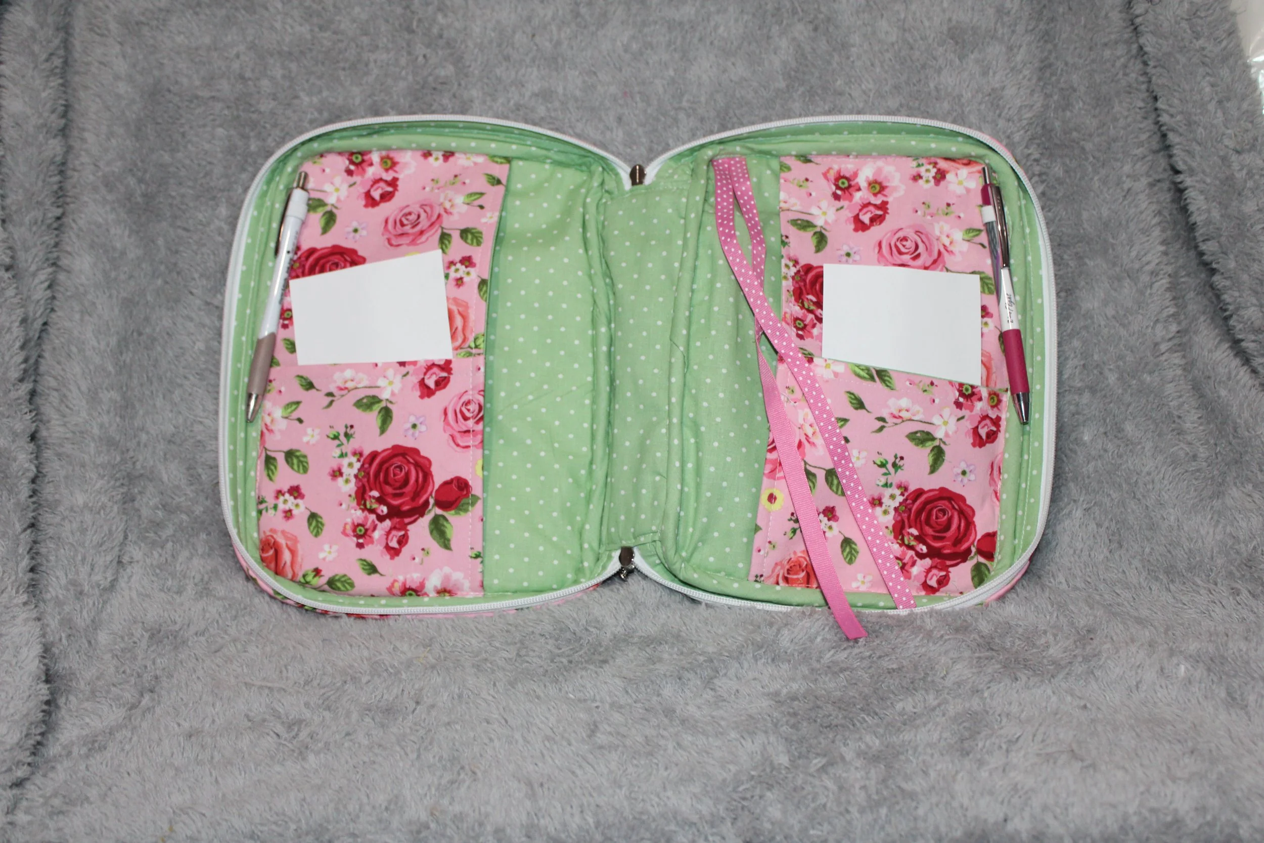 Empty interior view of the Roselyn pink quilted double‑zip Bible case showing green polka dot lining, pink rose fabric flaps, pen holders, and a pink polka dot ribbon.
