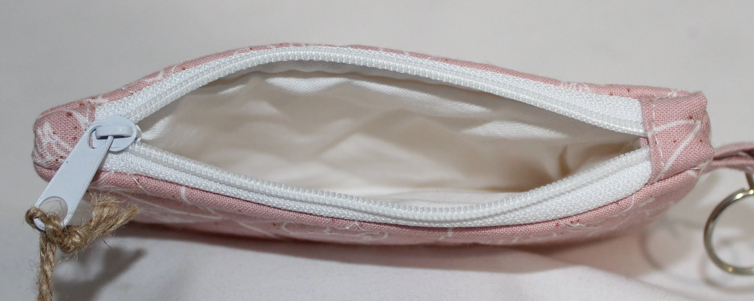 Top and interior view of zipper and white lining of small quilted keychain with a pink background and white floral design, zipper closure, and a key ring.