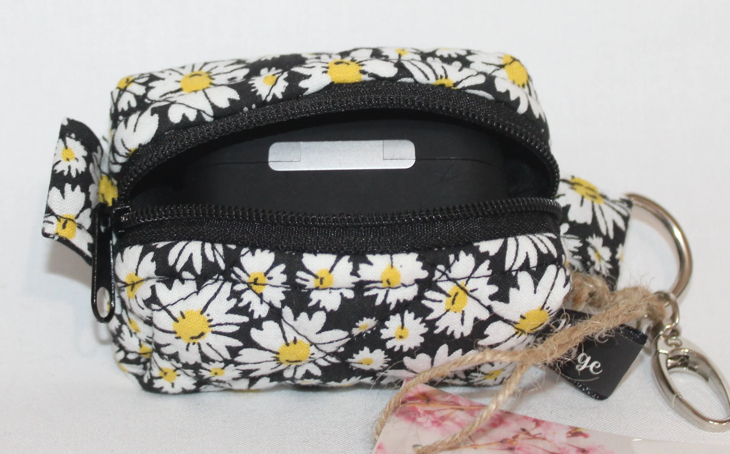 Top open view of the Ditzy Daisy Bag Charm showing zip enclosure and an Airpod Pro case inserted for size reference.