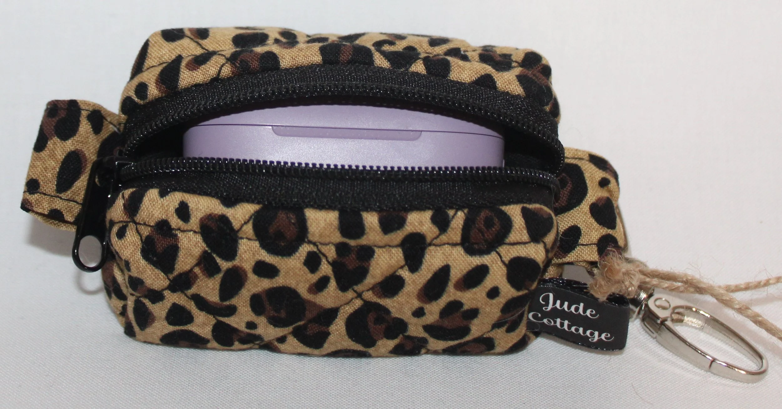 Top open view of the Sahara Bag Charm featuring cheetah print fabric with a set of J Lab earbuds inserted for size reference.