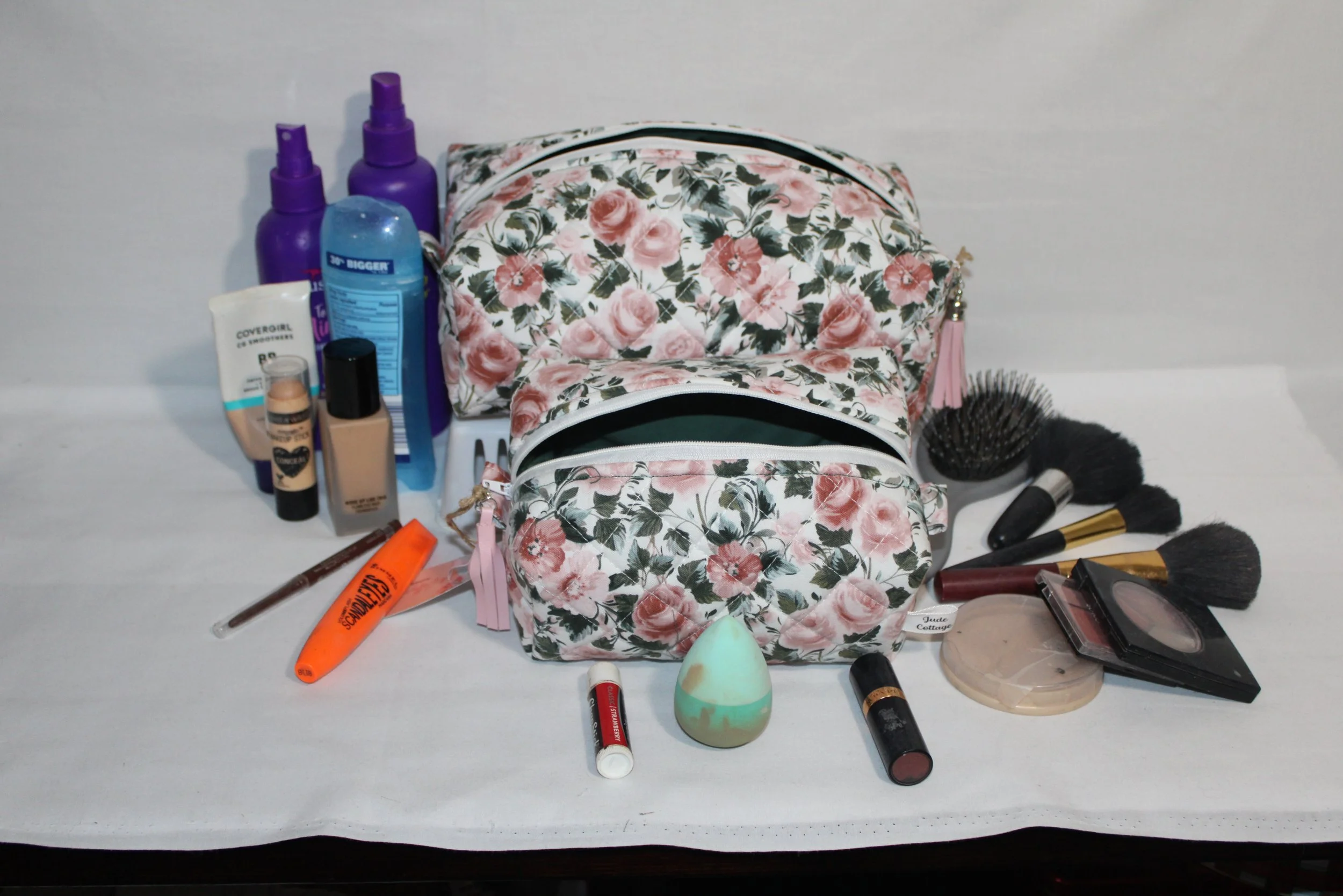 Angled front view of the large and small Rose Garden quilted travel pouches shown with open zipper to reveal dark green lining.