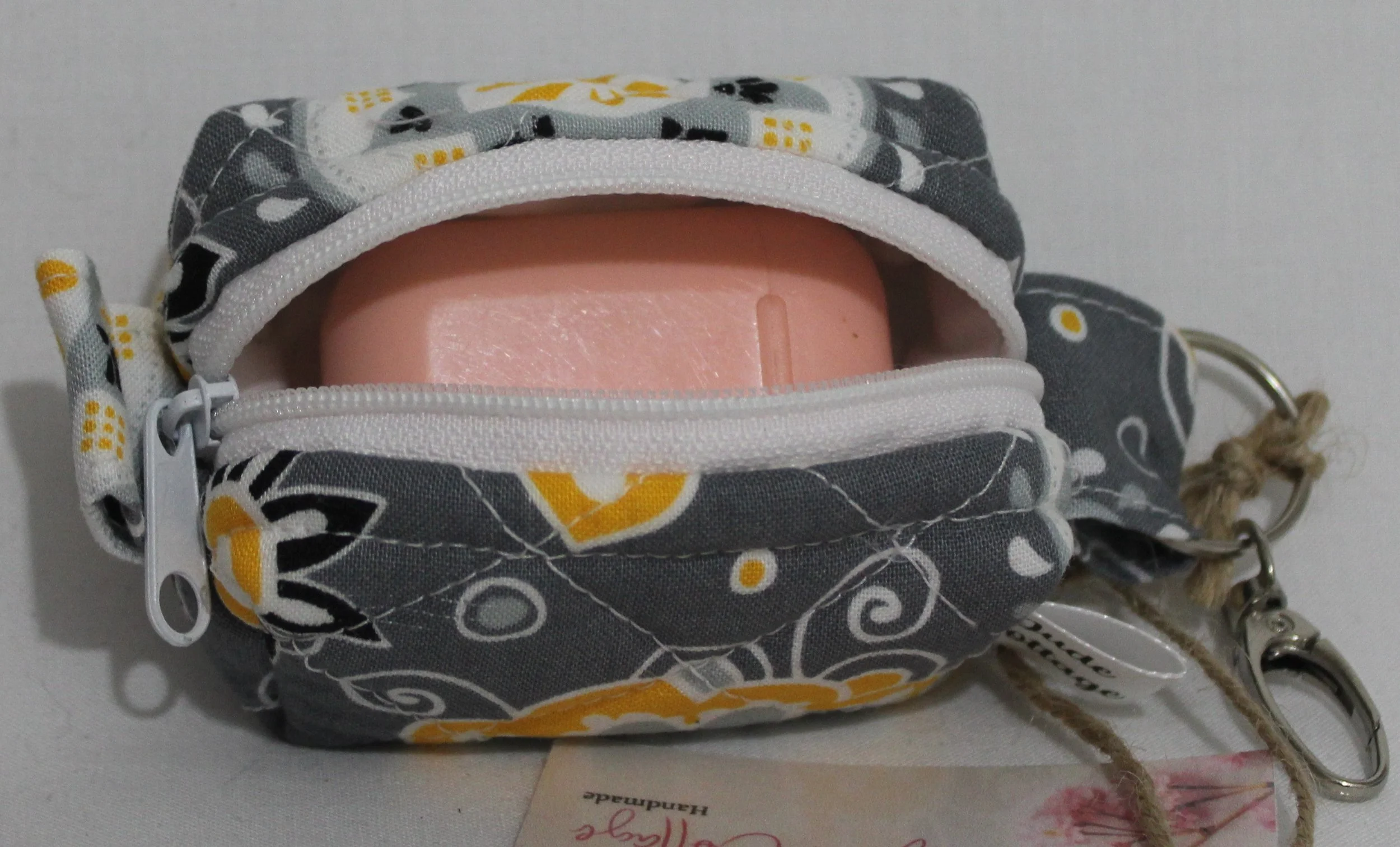 Top open view of the Medallion Bag charm featuring gray fabric with black, white and yellow floral print shown with an Airpod case inserted for sizing reference.