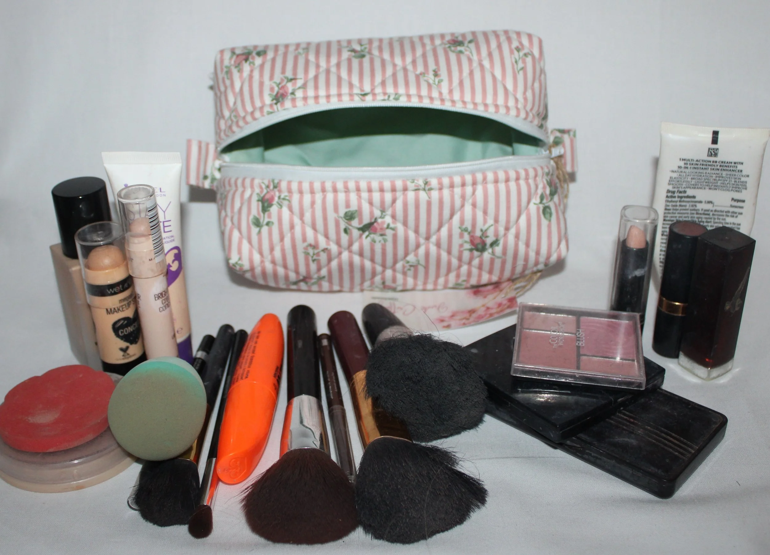 Top angled view of the small Victoria quilted travel pouch in pink floral stripe print displayed with cosmetics arranged around it to show size.