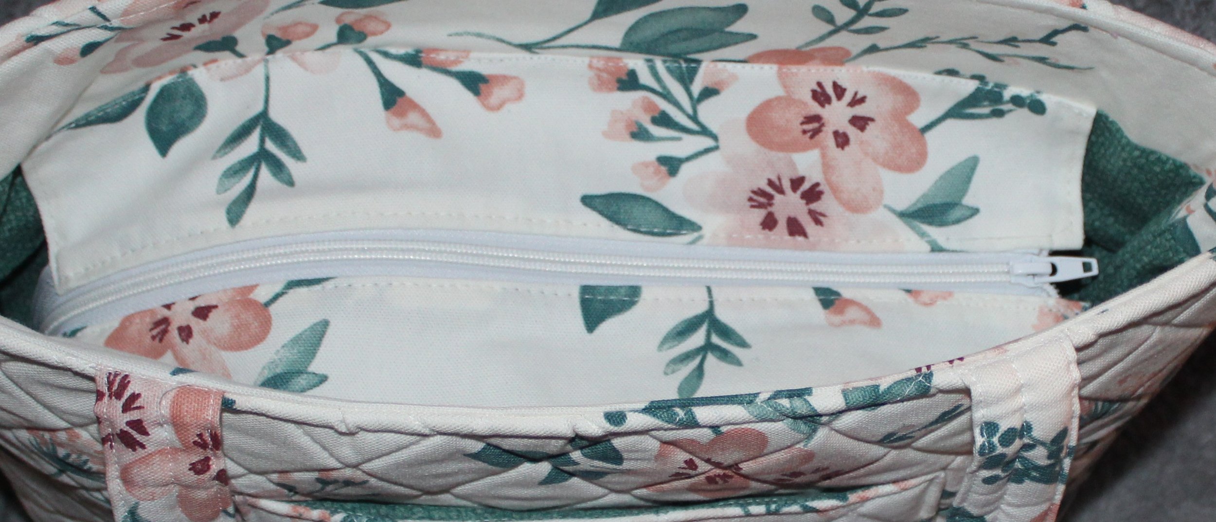 Top view of the Odette quilted tote in white fabric with a pink floral pattern, shown with the recessed zipper fully closed and the two padded shoulder straps visible.