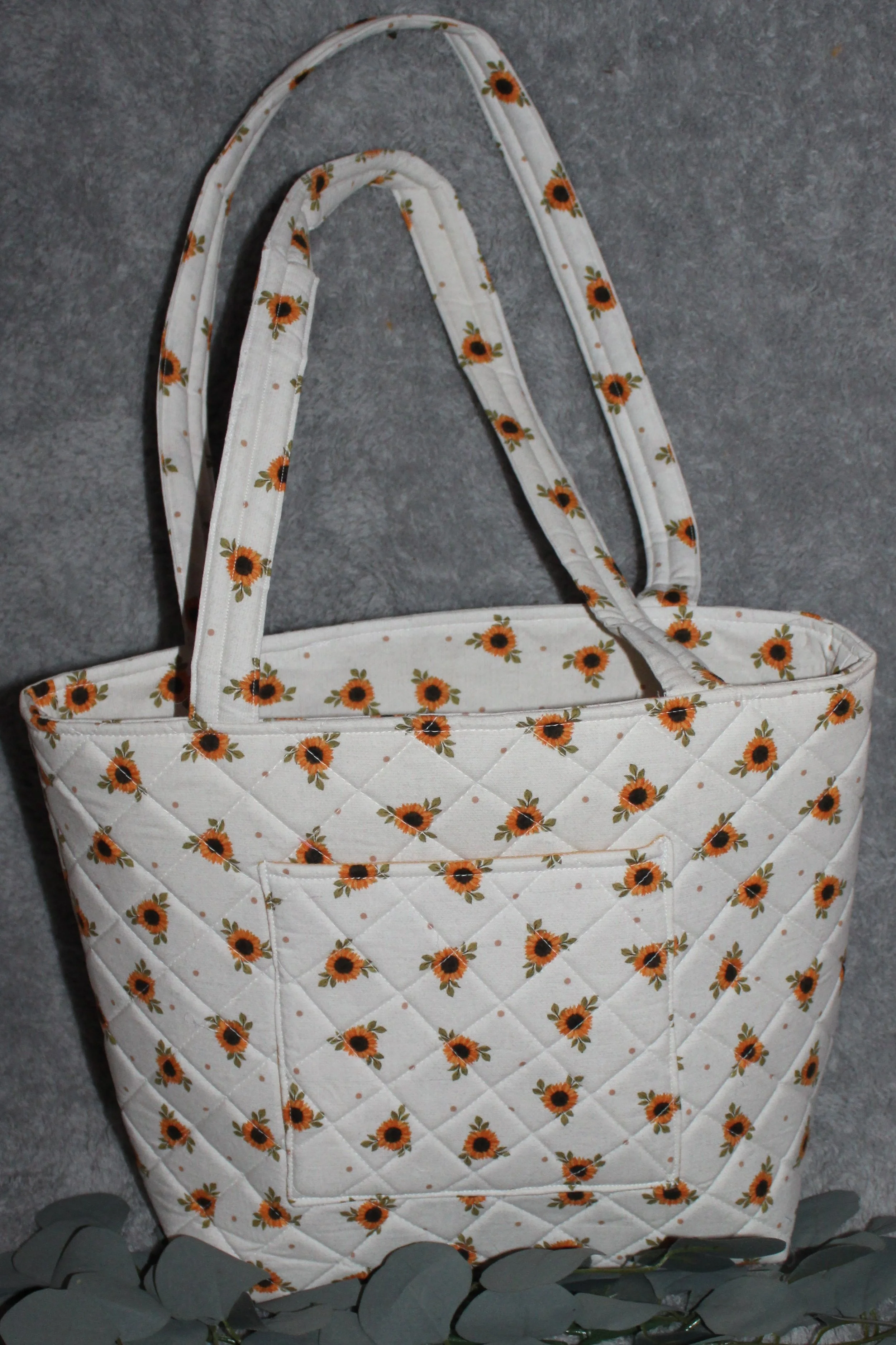 Back view of the Sunflower Medley quilted tote in white fabric with a dainty sunflower floral pattern, showing the quilted exterior, two padded shoulder straps, and one exterior slip pocket.