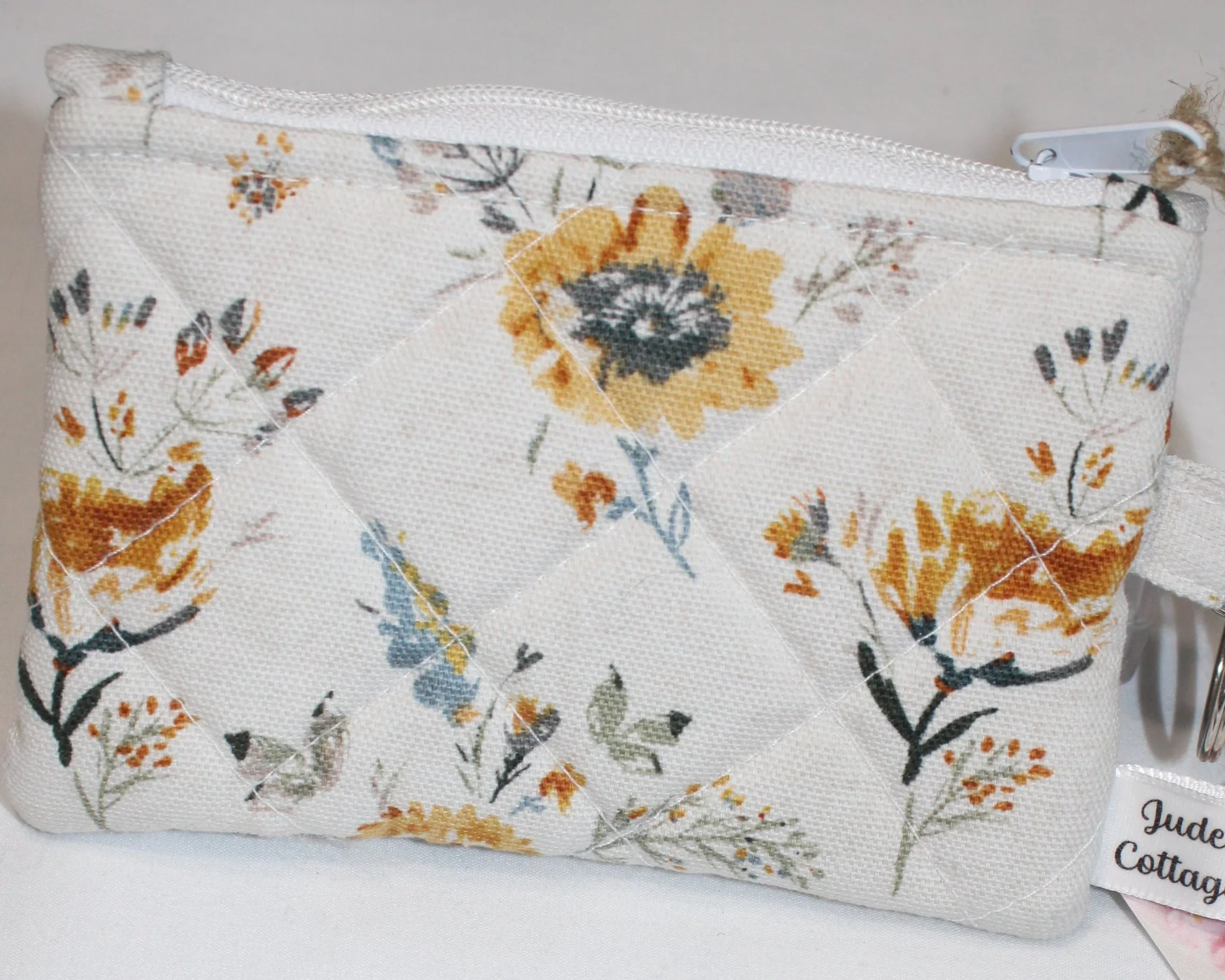 Floral quilted wallet with a white zipper and wildflower print in yellow, orange, blue, and green.