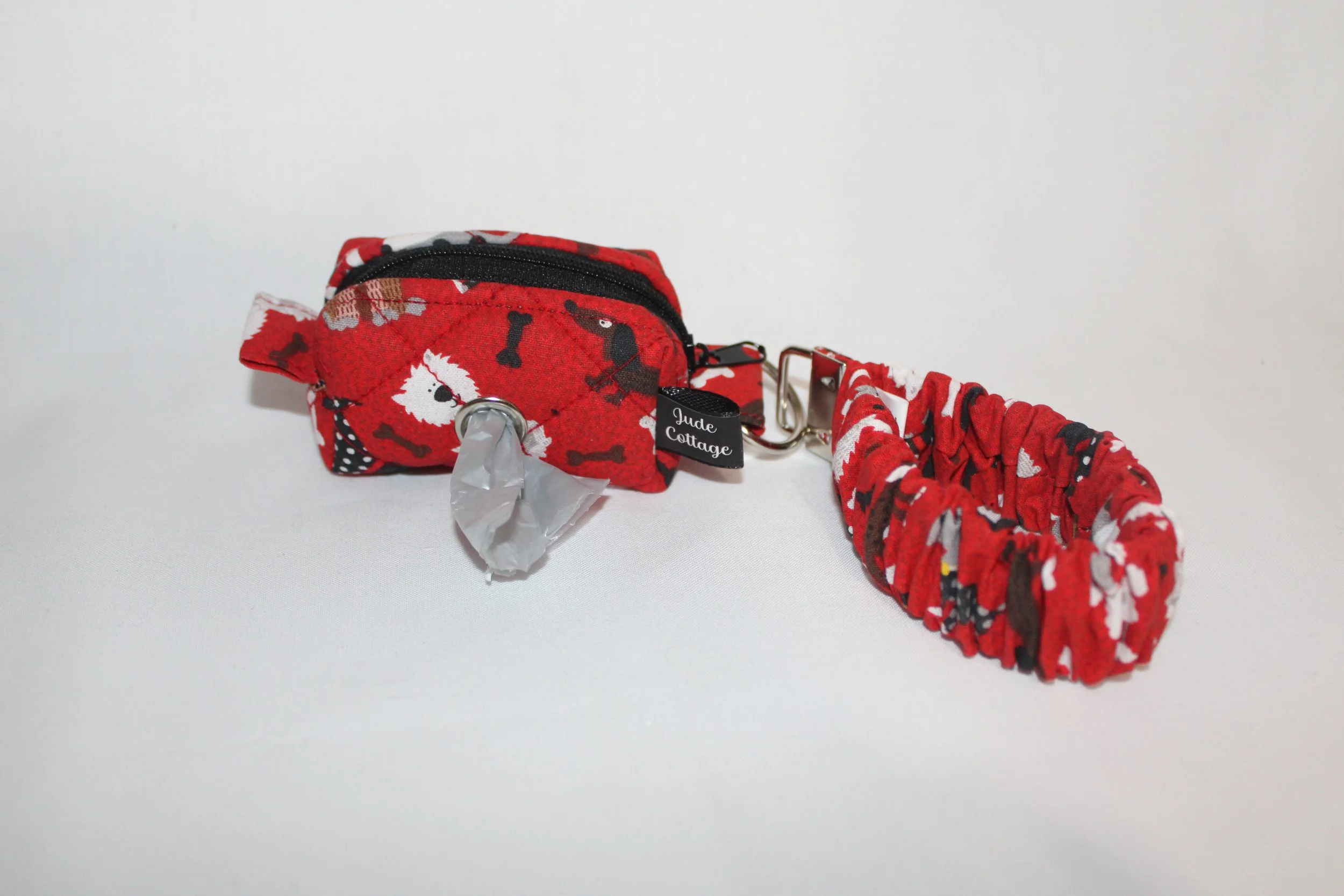Closed view of the Scarlet Dog mini boxy pouch in red fabric with dogs and bones pattern, with the matching scrunchie wristlet attached to the metal clip.