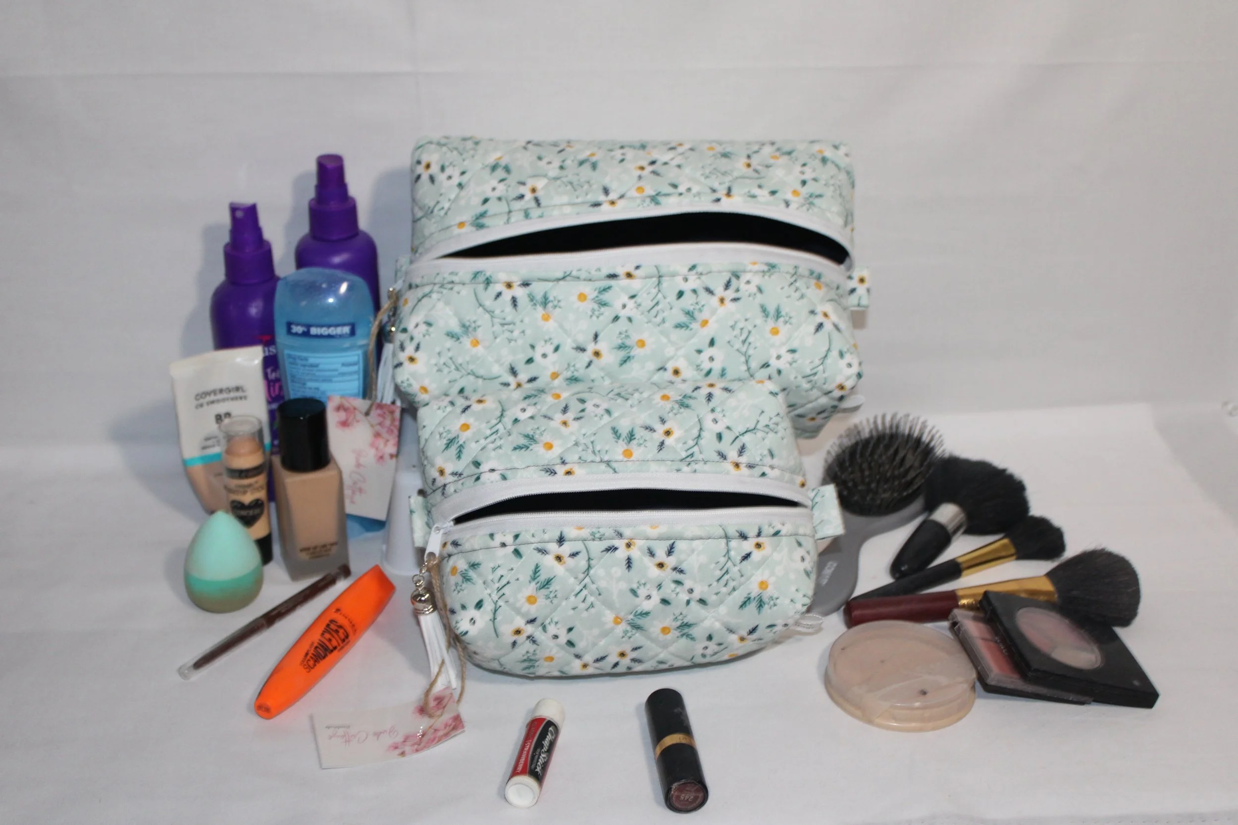 Large and small Vera travel cases in light blue floral quilted print displayed open with the navy lining showing and assorted cosmetics arranged around them.