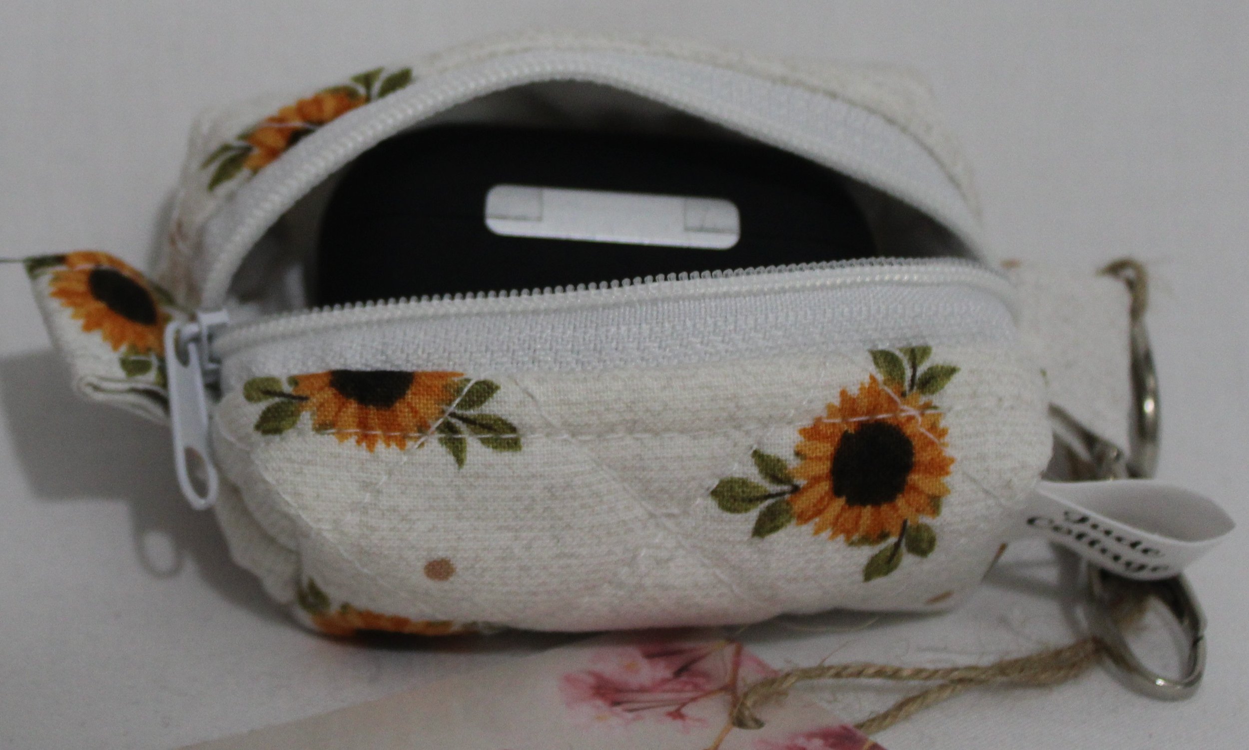 Open top view of the Sunflower Medley Bag Charm featuring small sunflowers on a cream background shown with a set of Airpod Pro earbuds inserted for size demonstration..