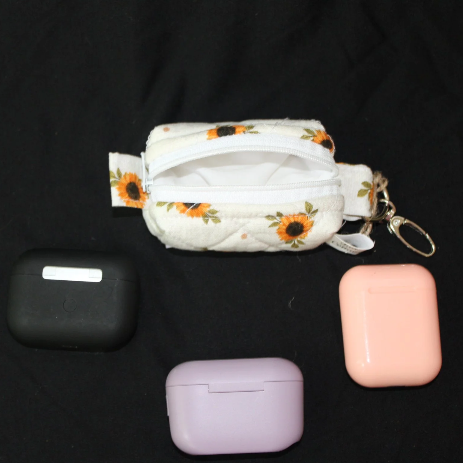 Top view of the Sunflower Medley Bag Charm featuring small sunflowers on a cream background shown with three different sized earbud cases for sizing reference.