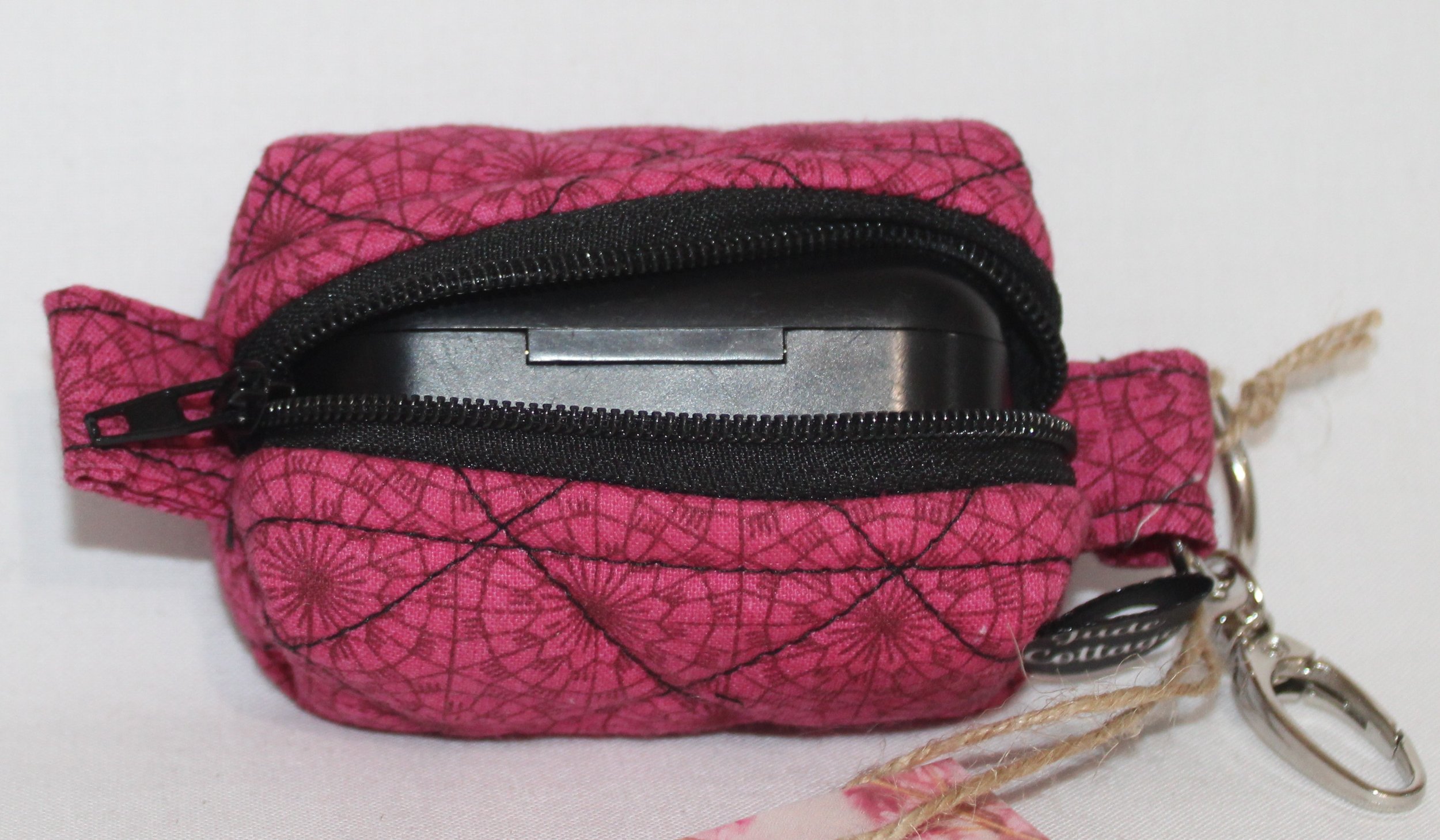 Front view of the Claire Bag Charm featuring a dark pink fabric with geometric print shown with a J Lab earbud case inserted to show sizing.
