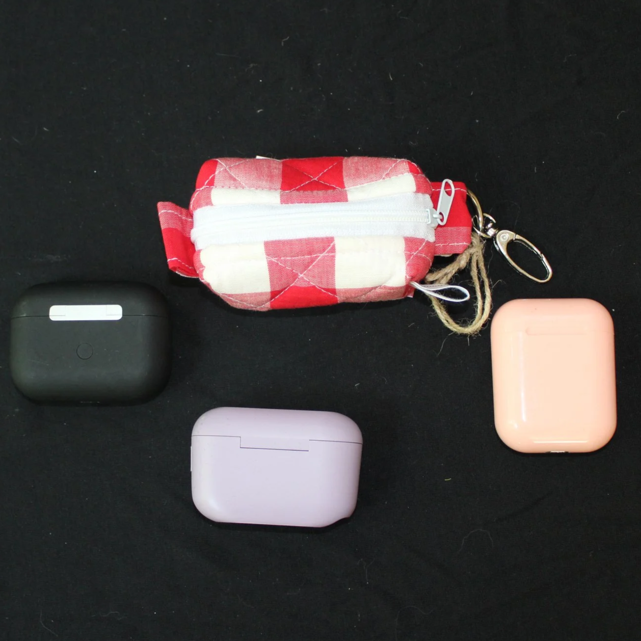 Top closed view of the Stella Bag Charm featuring a red and white plaid fabric shown with different sized earbud cases for sizing reference.