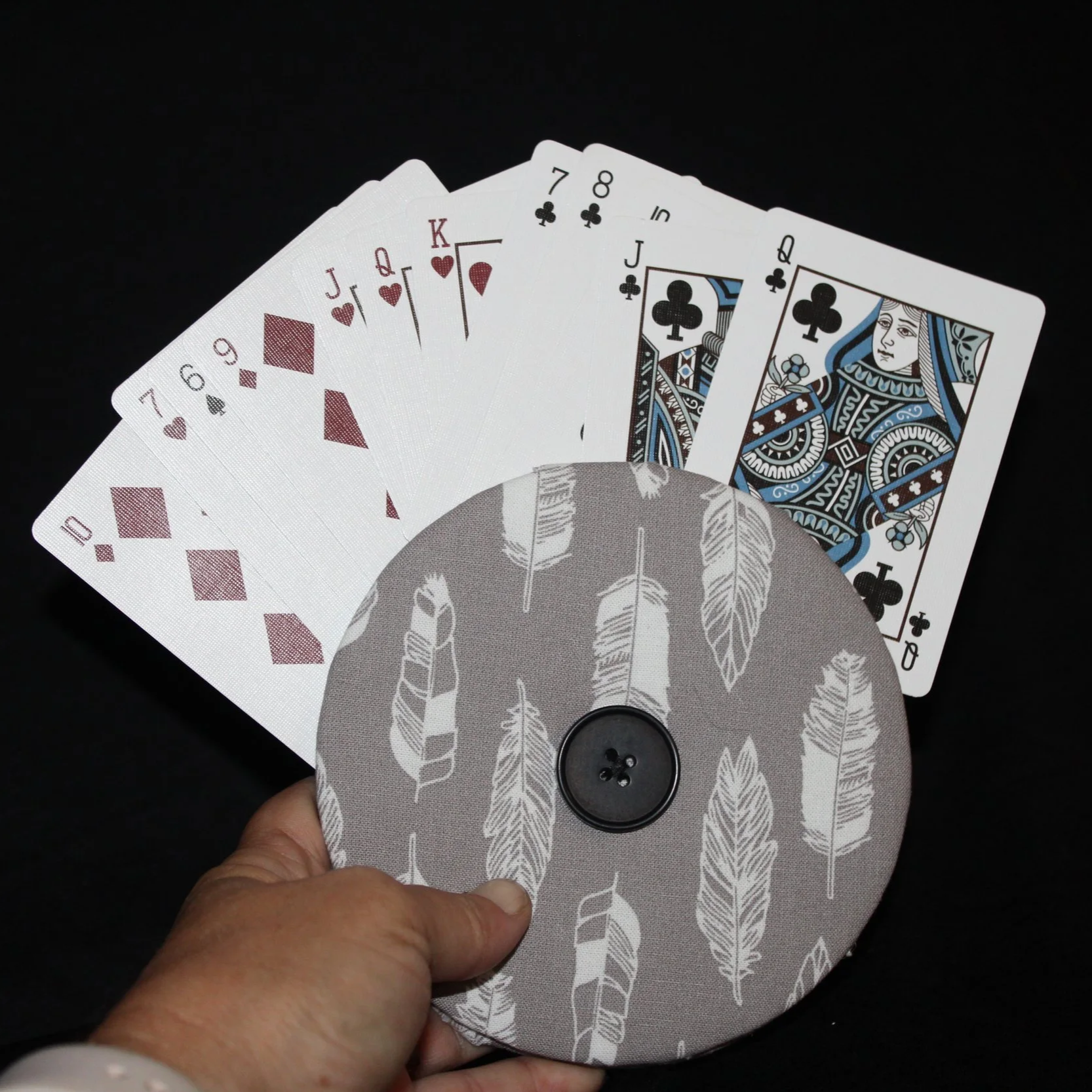 Front view of the Grey Feather Card Holder featuring a grey background with white feather motif print fabric shown in use being held with an array of playing cards.