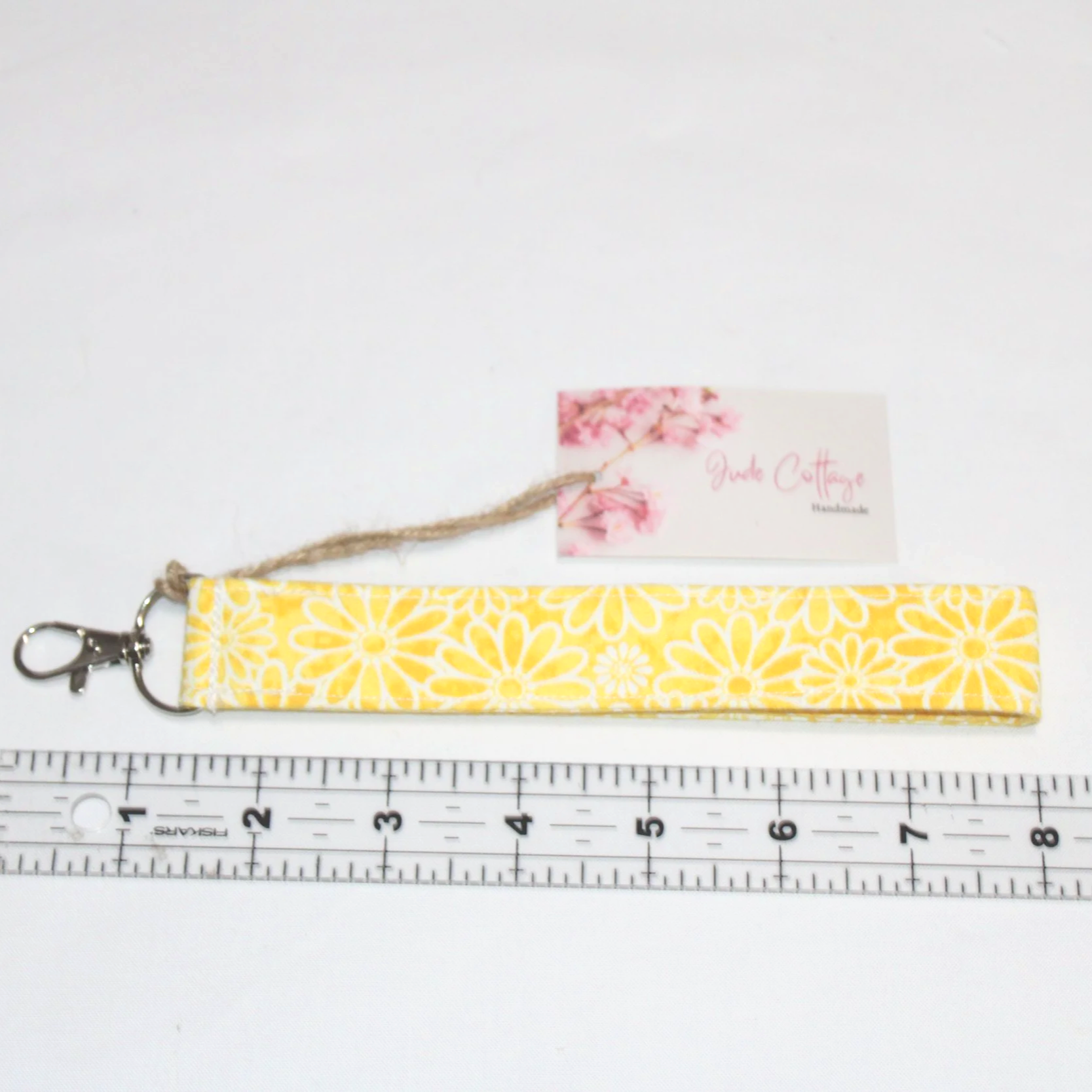 Close up view of the Gold Daisy Wristlet showing the bright yellow and white daisy pattern and lobster clip pictured above a ruler to demonstrate sizing..