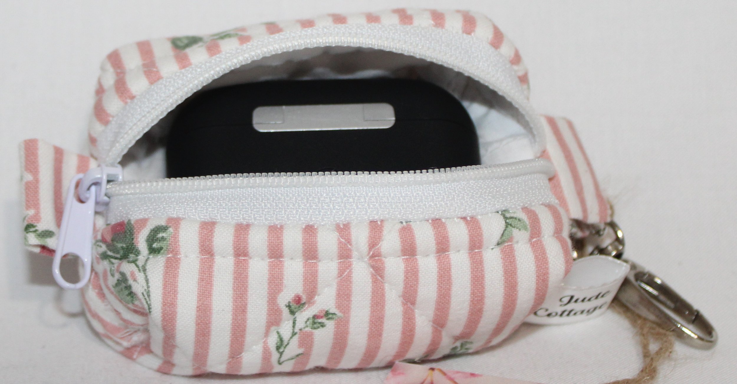 Open top view of the Victoria bag charm featuring pink and white stripes with pink rose bud printed fabric shown with a set of Airpod Pro earbuds inserted for sizing reference.