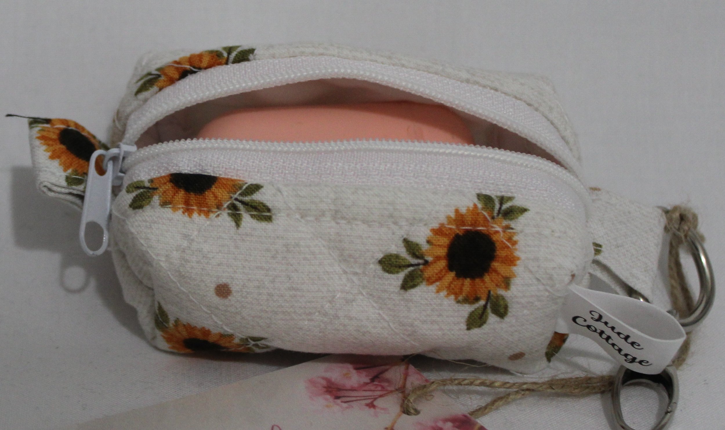 Open top view of the Sunflower Medley Bag Charm featuring small sunflowers on a cream background shown with a set of Airpods inserted for size demonstration..
