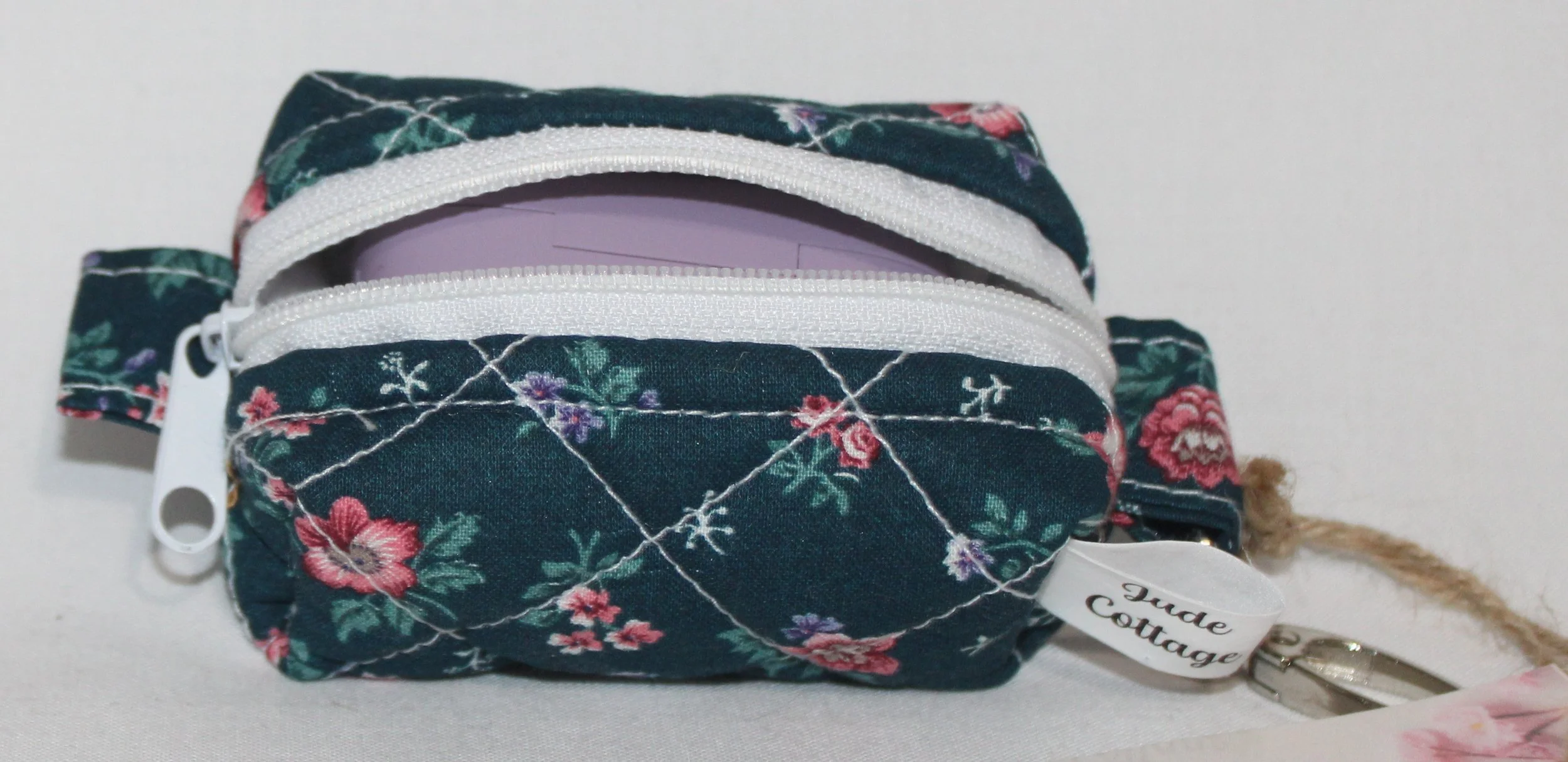 Open top view of the Eliza Bag Charm featuring a dark teal background with pink and lilac floral print shown with a J Lab earbud case inserted demonstrating size.