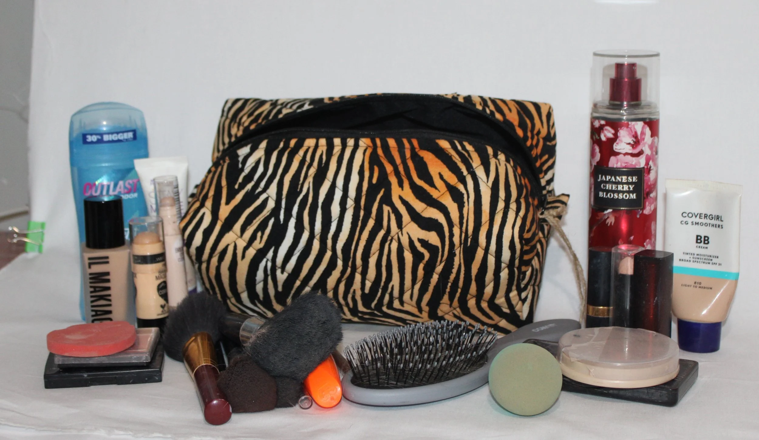 Angled front view of the Zara tiger‑print quilted travel bag with black zipper open showing black lining, pictured with cosmetic items to show size and use.