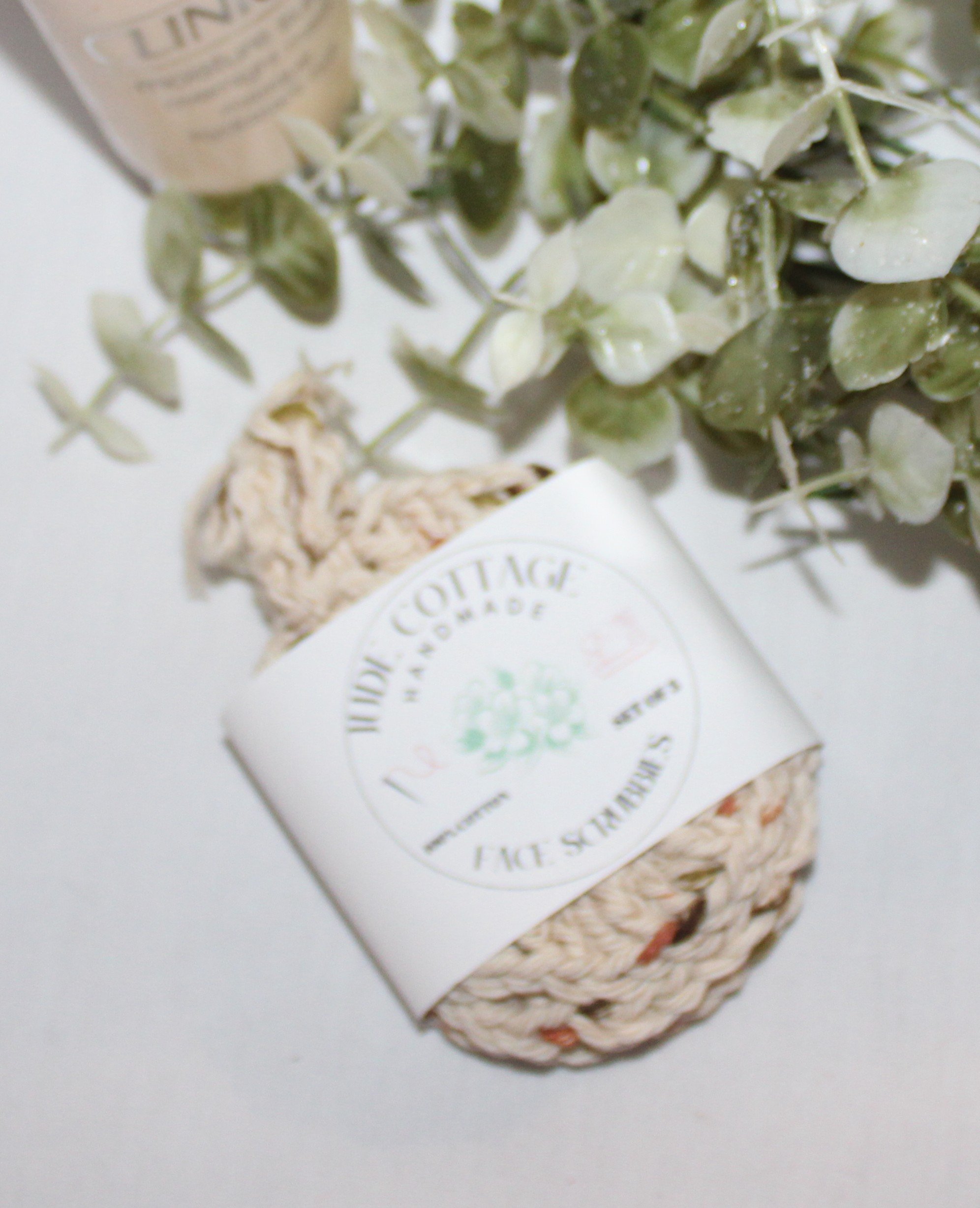 Close‑up of round crocheted beige facial scrubbies with a textured stitch pattern shown with label.