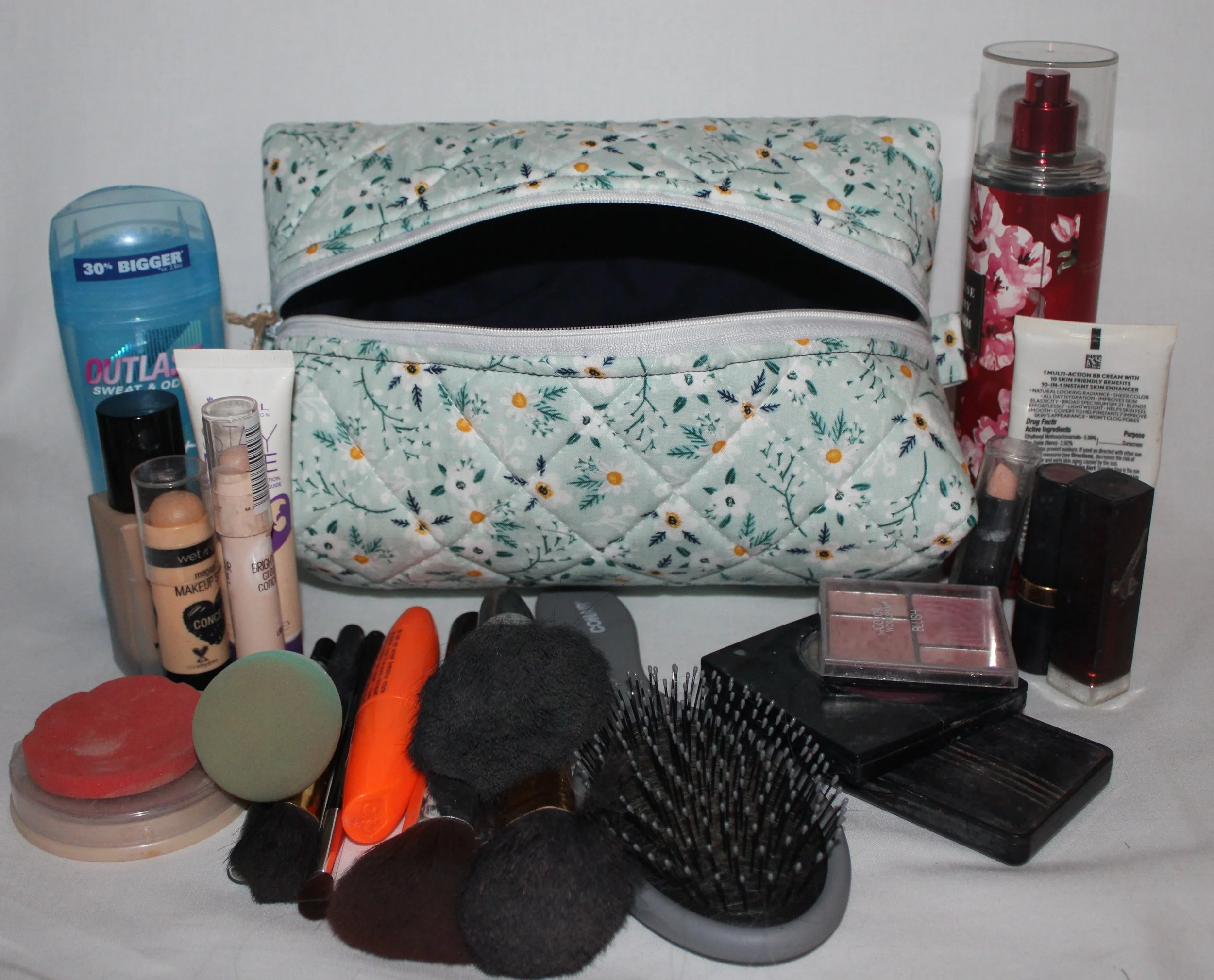 Large Vera travel case in light blue floral quilted print displayed open with the navy lining showing and assorted cosmetics arranged around them.