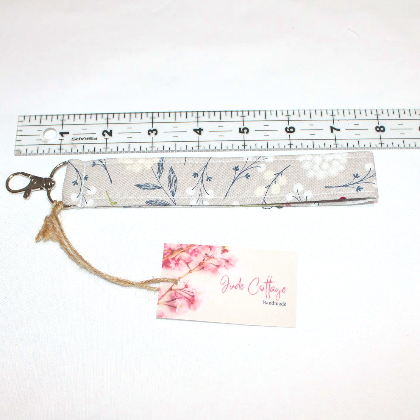 Dandelion Field Wristlet in grey and white dandelion‑print fabric with an approximately 7.5‑inch strap and metal clasp, displayed on a simple background, shown with ruler to demonstrate size.