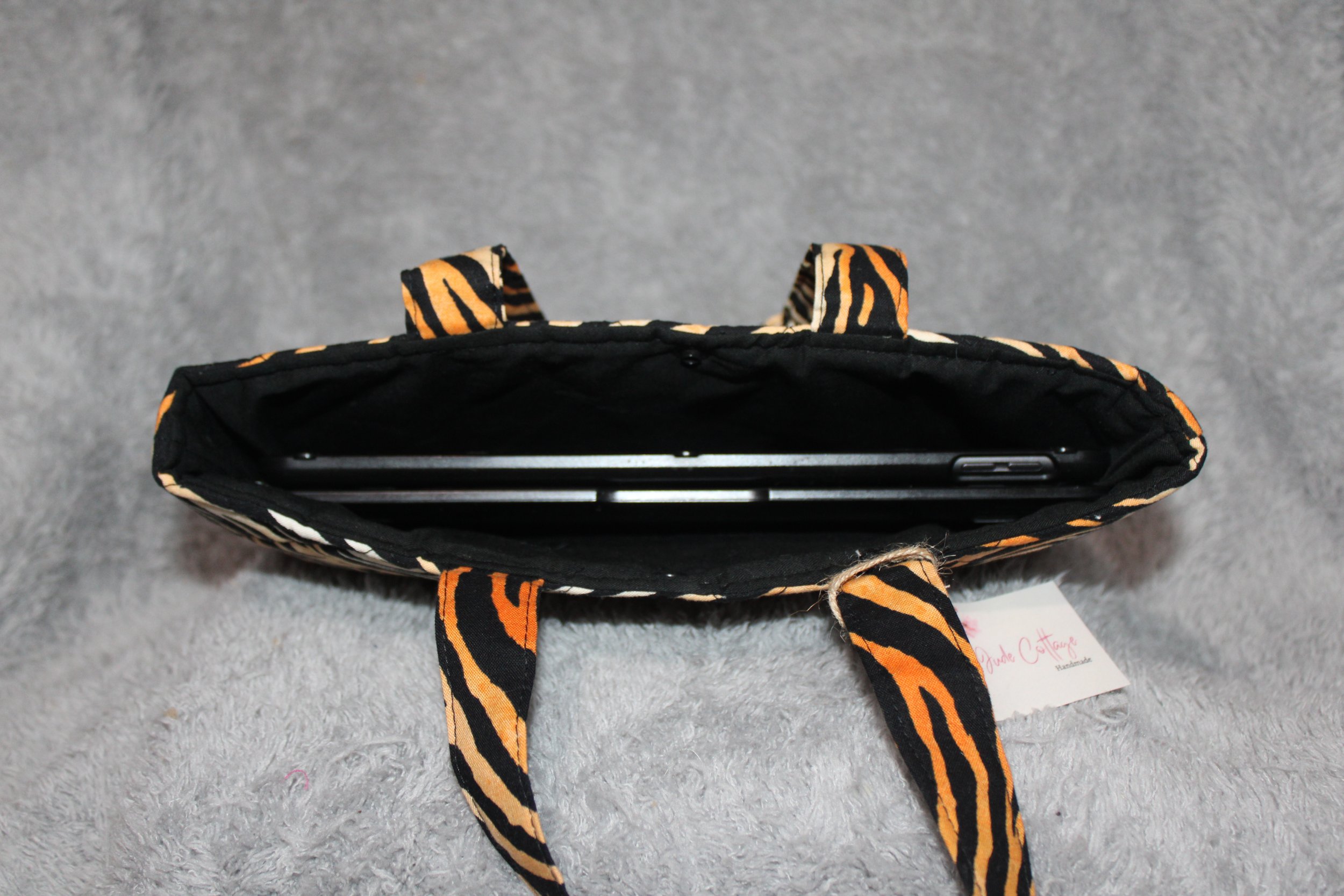 Top view of the Zara quilted tiger‑print tablet sleeve with two carry handles, a snap closure, and a tablet inserted.