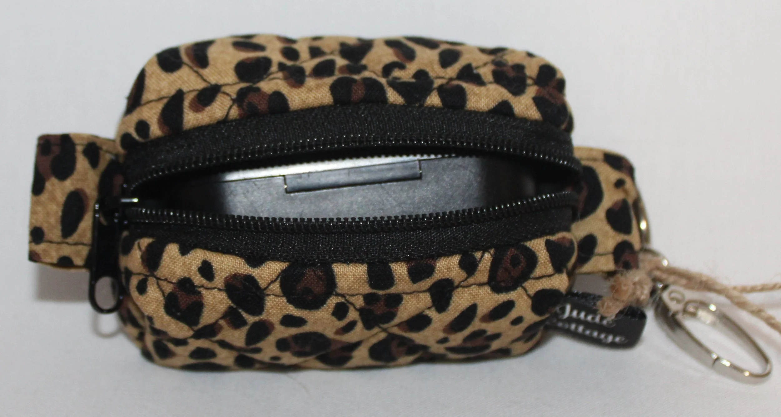 Top open view of the Sahara Bag Charm featuring cheetah print fabric with a set of J Lab earbuds inserted for size reference.