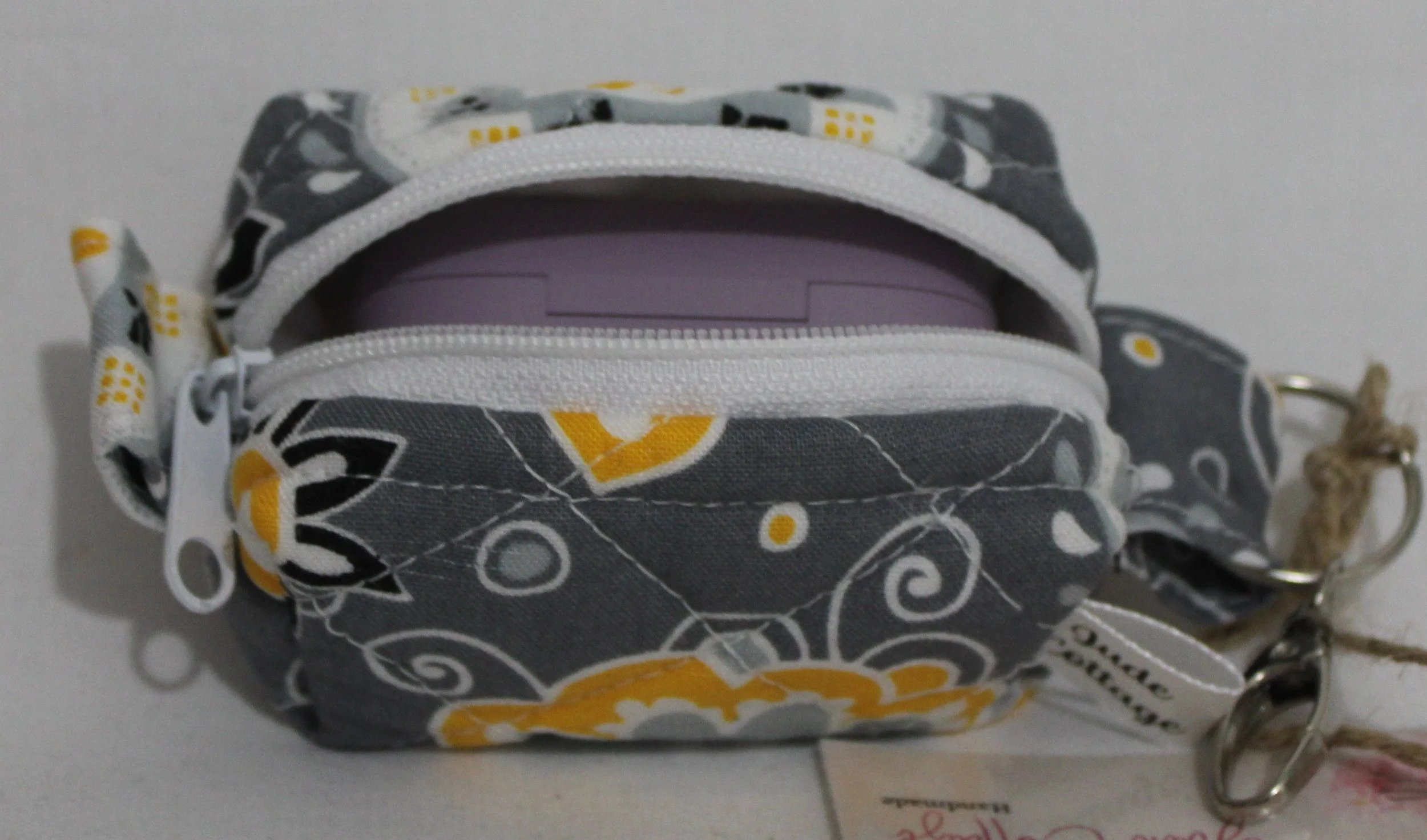 Top open view of the Medallion Bag charm featuring gray fabric with black, white and yellow floral print shown with an J Lab earbud case inserted for sizing reference.