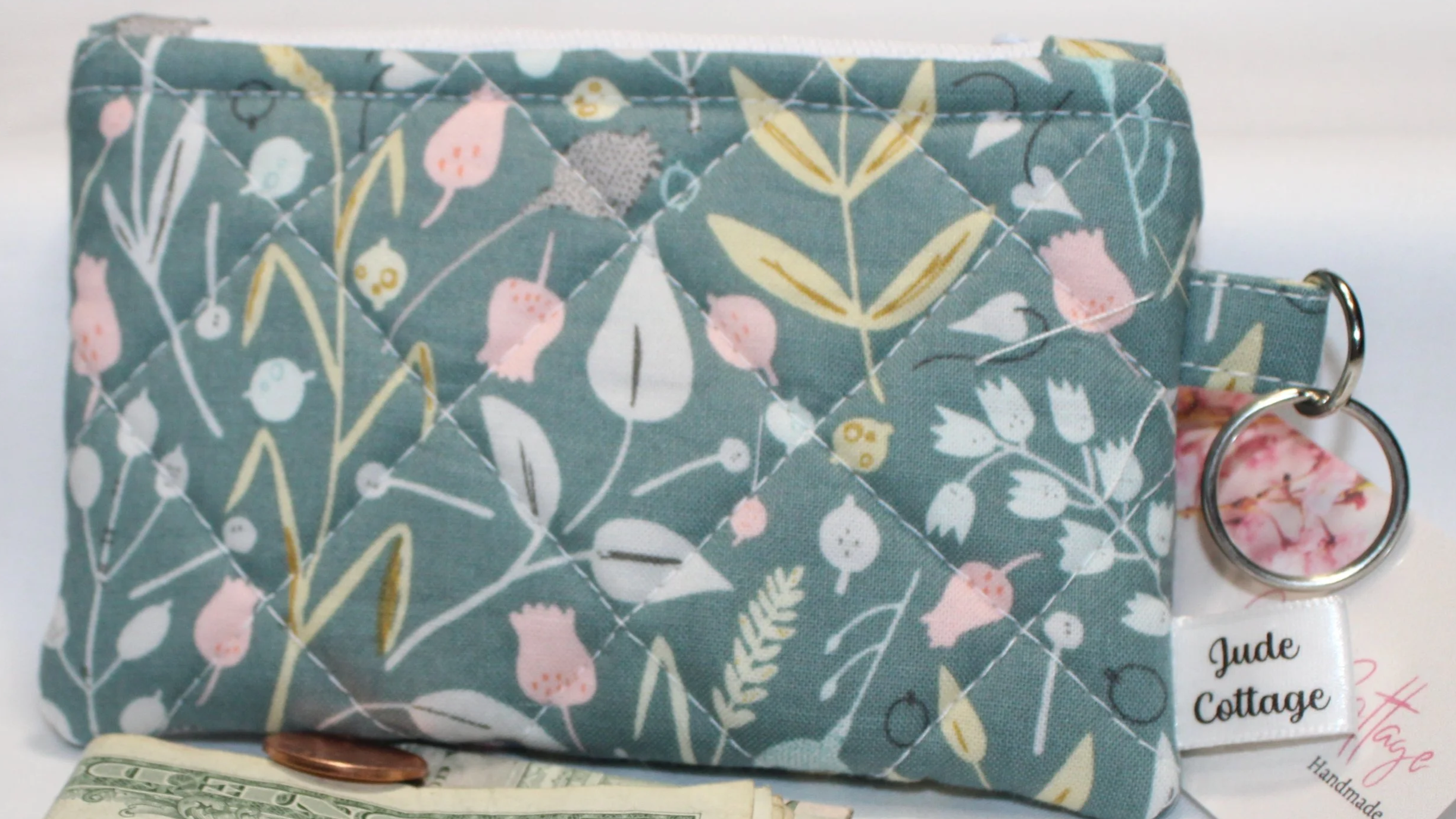 Close up view of the Meadow Breeze, with a soft green quilted keychain wallet with meadow floral pattern, zipper closure, and metal key ring.