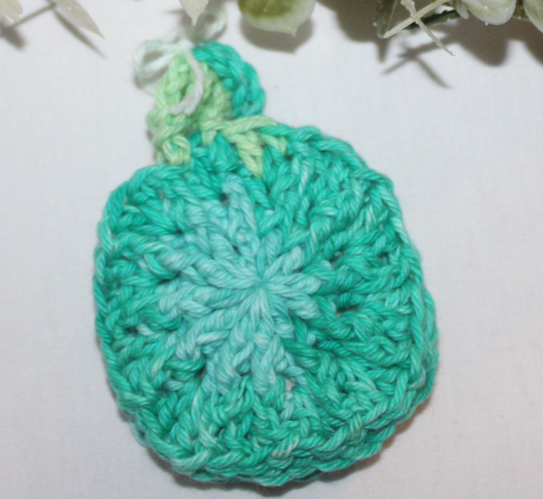 Close-up view of crocheted face scrubbies in assorted shades of green colors, arranged on a flat surface and show the texture.
