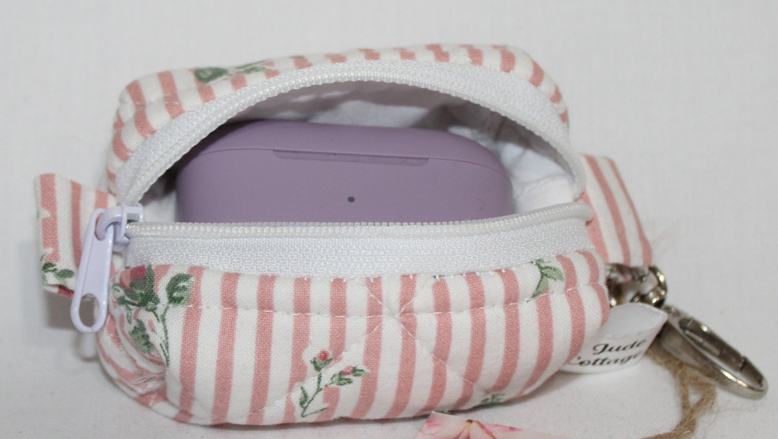Open top view of the Victoria bag charm featuring pink and white stripes with pink rose bud printed fabric shown with a set of J Lab earbuds inserted for sizing reference.