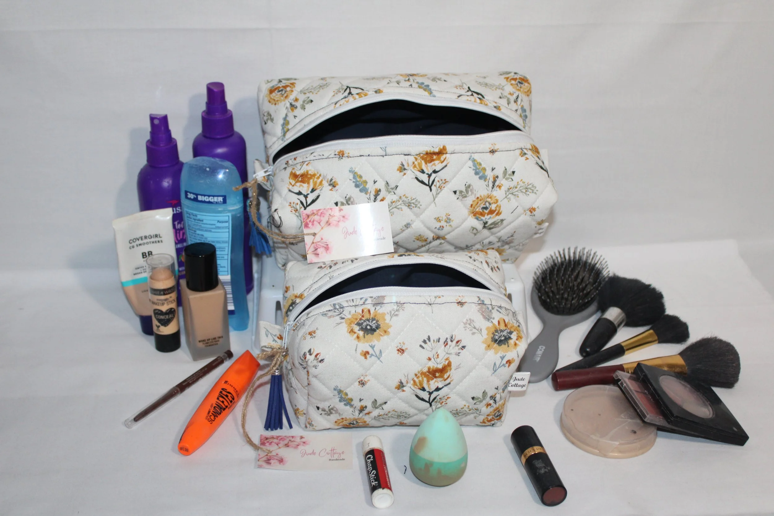 Large and small Dandelion Blue quilted travel pouches in blue and yellow floral print displayed with assorted beauty products.