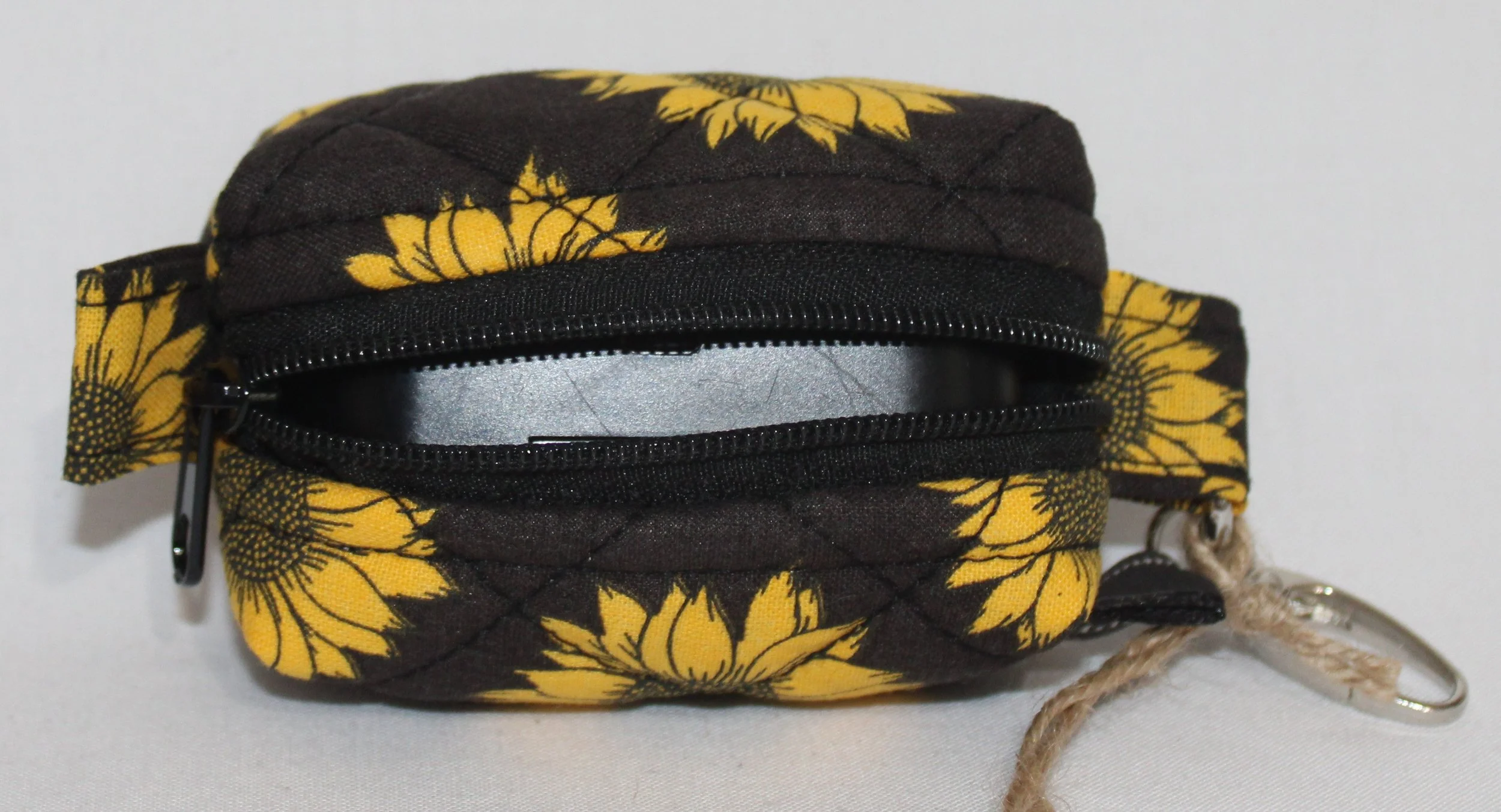 Top open view of the Midnight Sunflower Bag Charm featuring a black background fabric with bright golden yellow sunflowers, shown with a J Lab earbud case inserted to demonstrate fit.