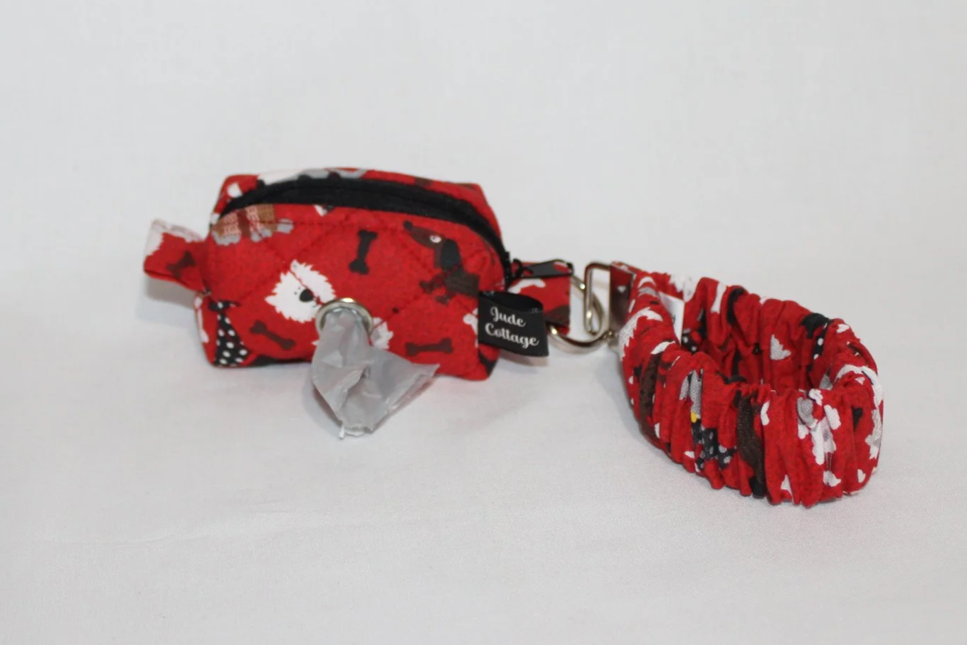 Closed view of the Scarlet Dog mini boxy pouch in red fabric with dogs and bones pattern, with the matching scrunchie wristlet attached to the metal clip.