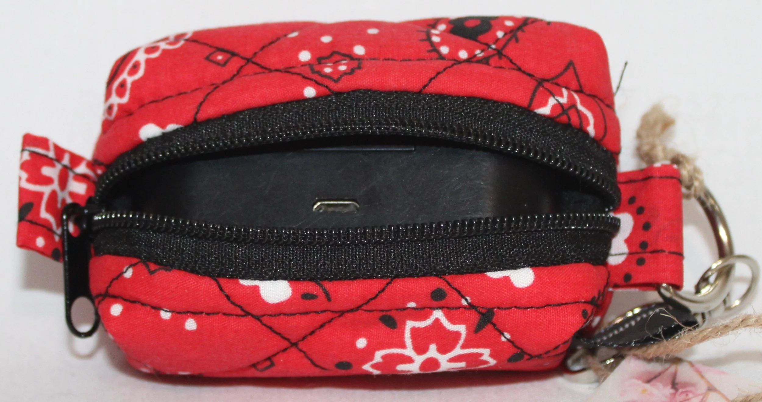 Top open view of the Red Bandana Bag Charm showing bandana print fabric with a set of J Lab earbuds inserted for size reference.