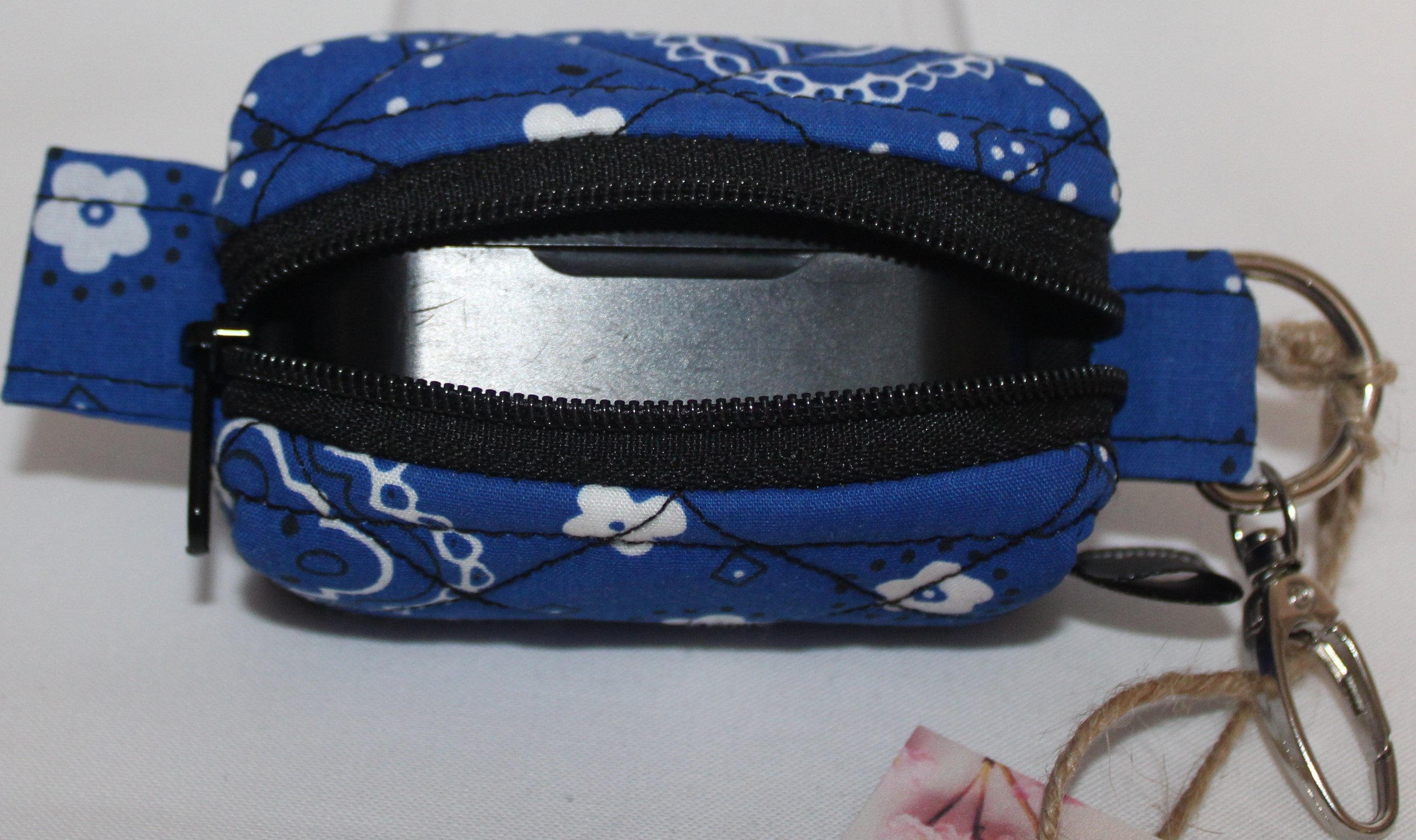 Top open view of the Blue Bandana Bag Charm showing its blue bandana‑print fabric with the zipper fully open. A pair of J Lap earbuds is placed inside the pouch for size and fit demonstration.