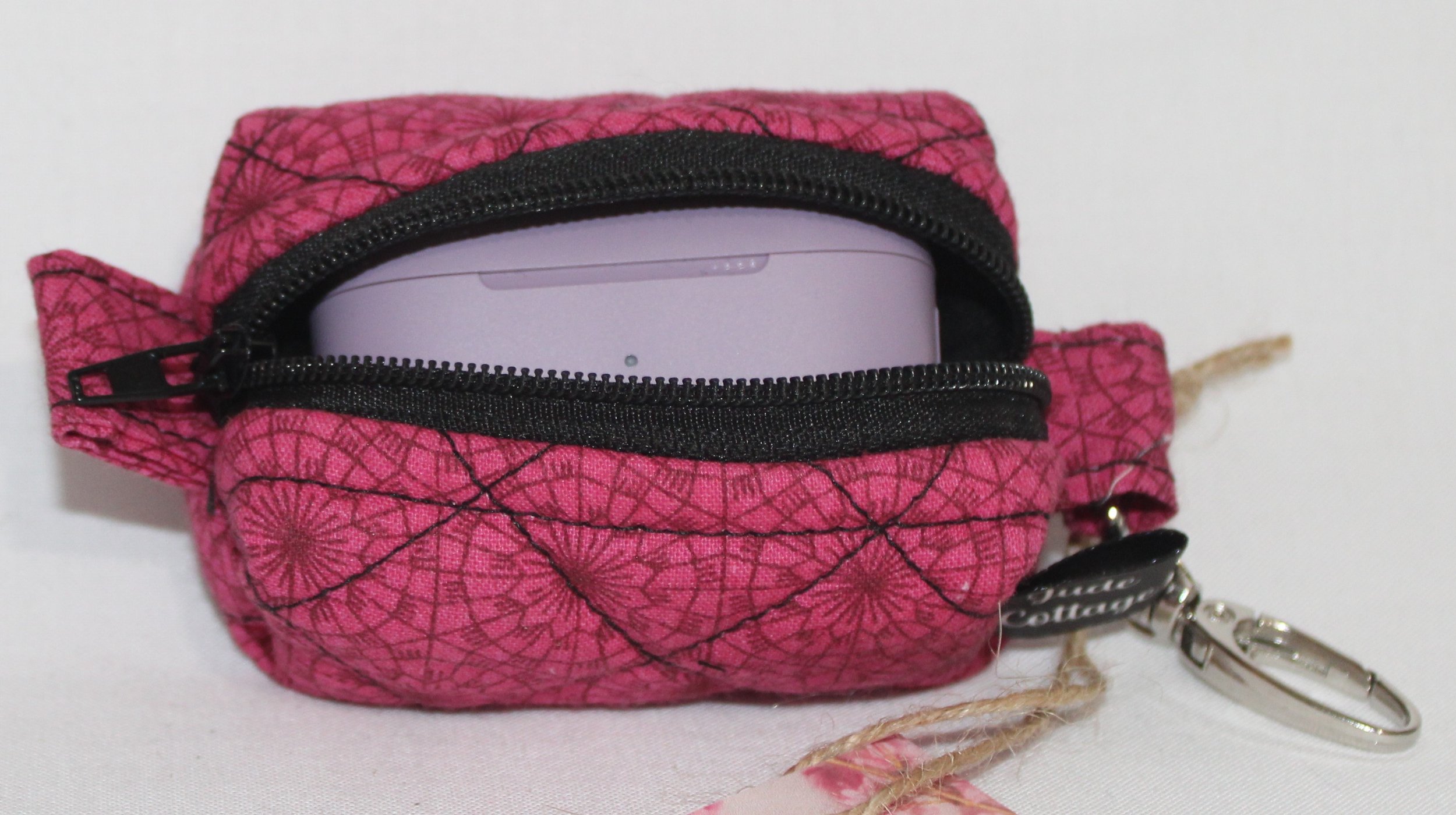 Front view of the Claire Bag Charm featuring a dark pink fabric with geometric print shown with a J Lab earbud case inserted to show sizing.