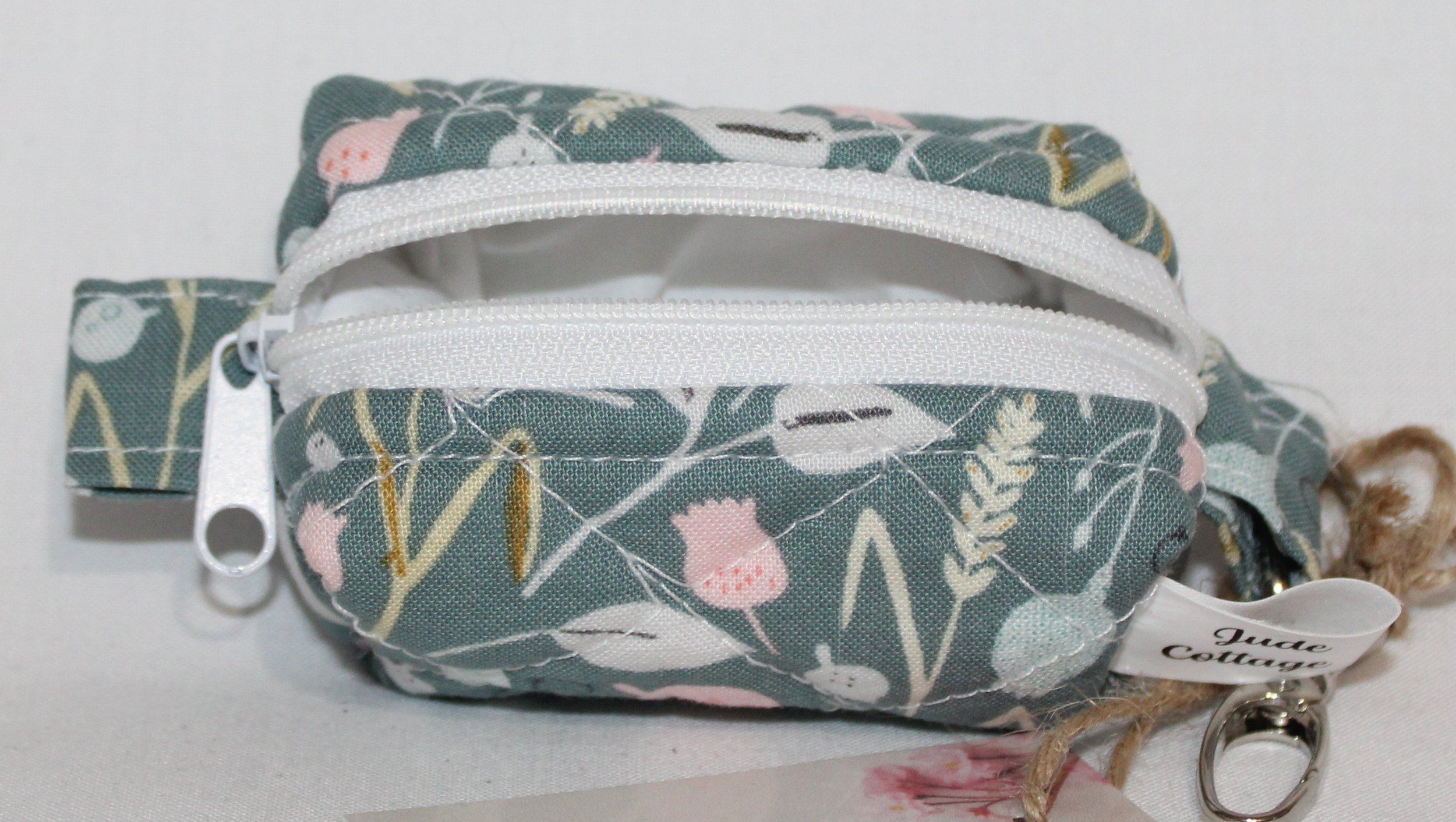 Open top view of the Meadow Breeze Bag Charm featuring a sage green background with spring floral print showing white zip closure and lining..