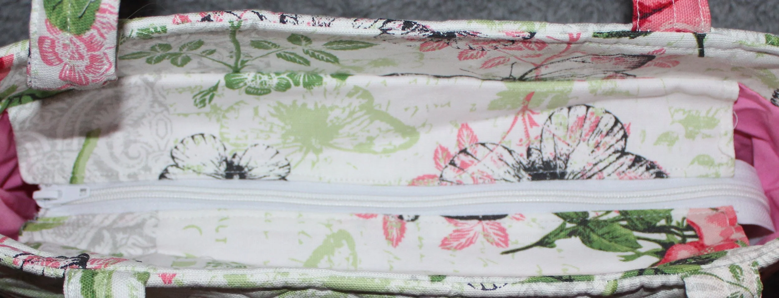 Top view of the Colette quilted tote in white fabric with a pink floral pattern, shown with the recessed zipper fully closed and the two padded shoulder straps visible.