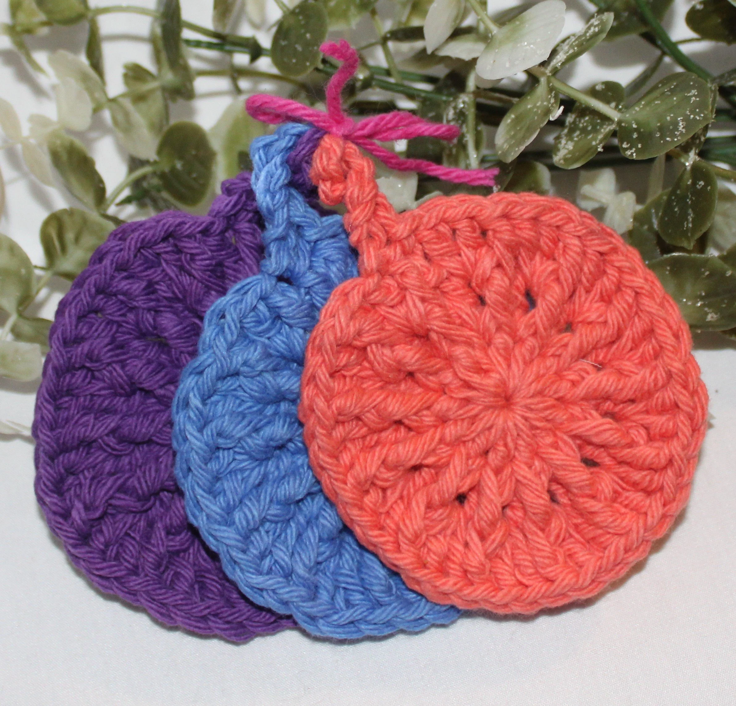 Close‑up of round crocheted assorted colors of blue plum coral facial scrubbies with a textured stitch pattern.