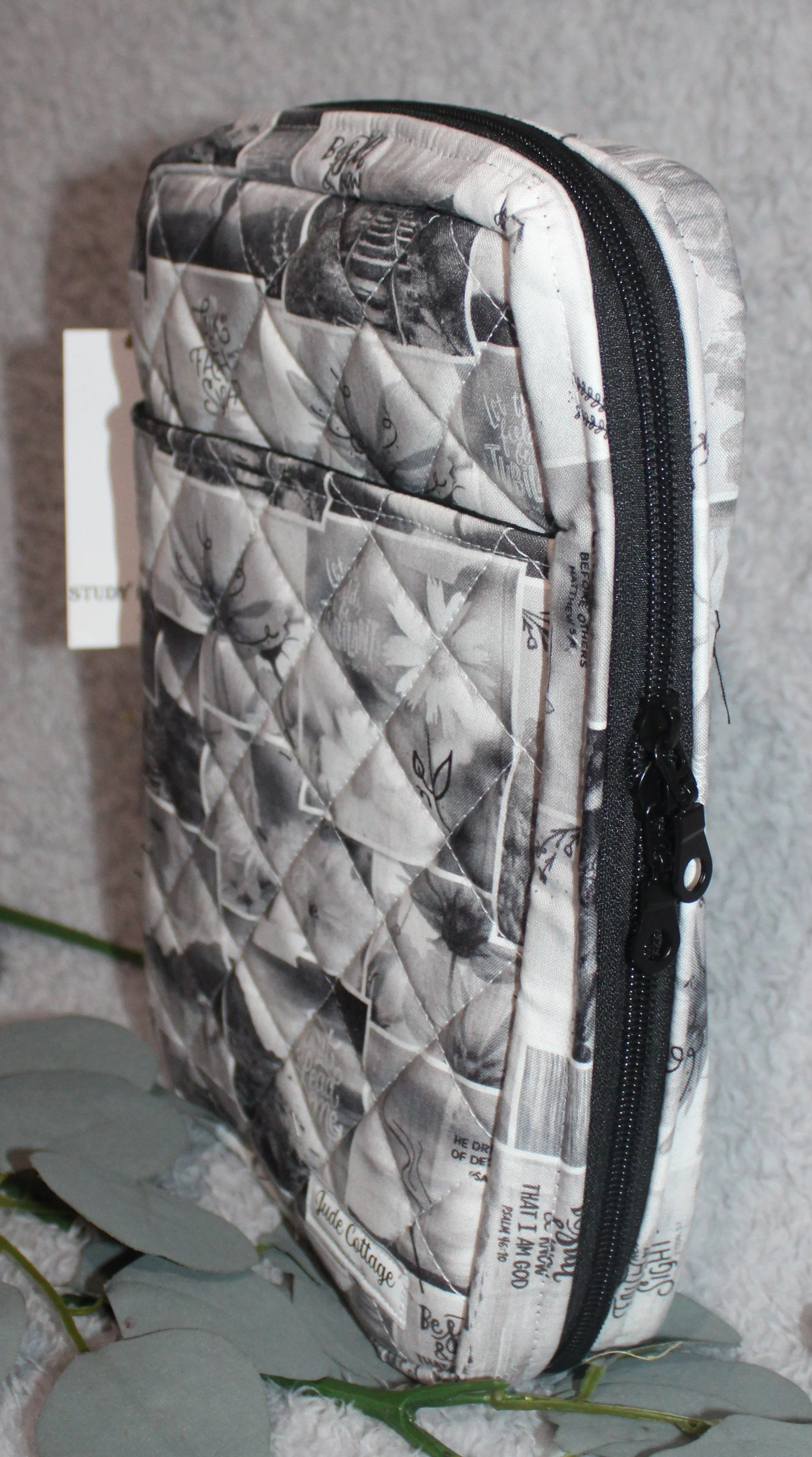 Calvary Study Bible Case with monochrome inspirational text and floral motifs, showing the front slip pocket, double‑zip enclosure, and quilted detail.
