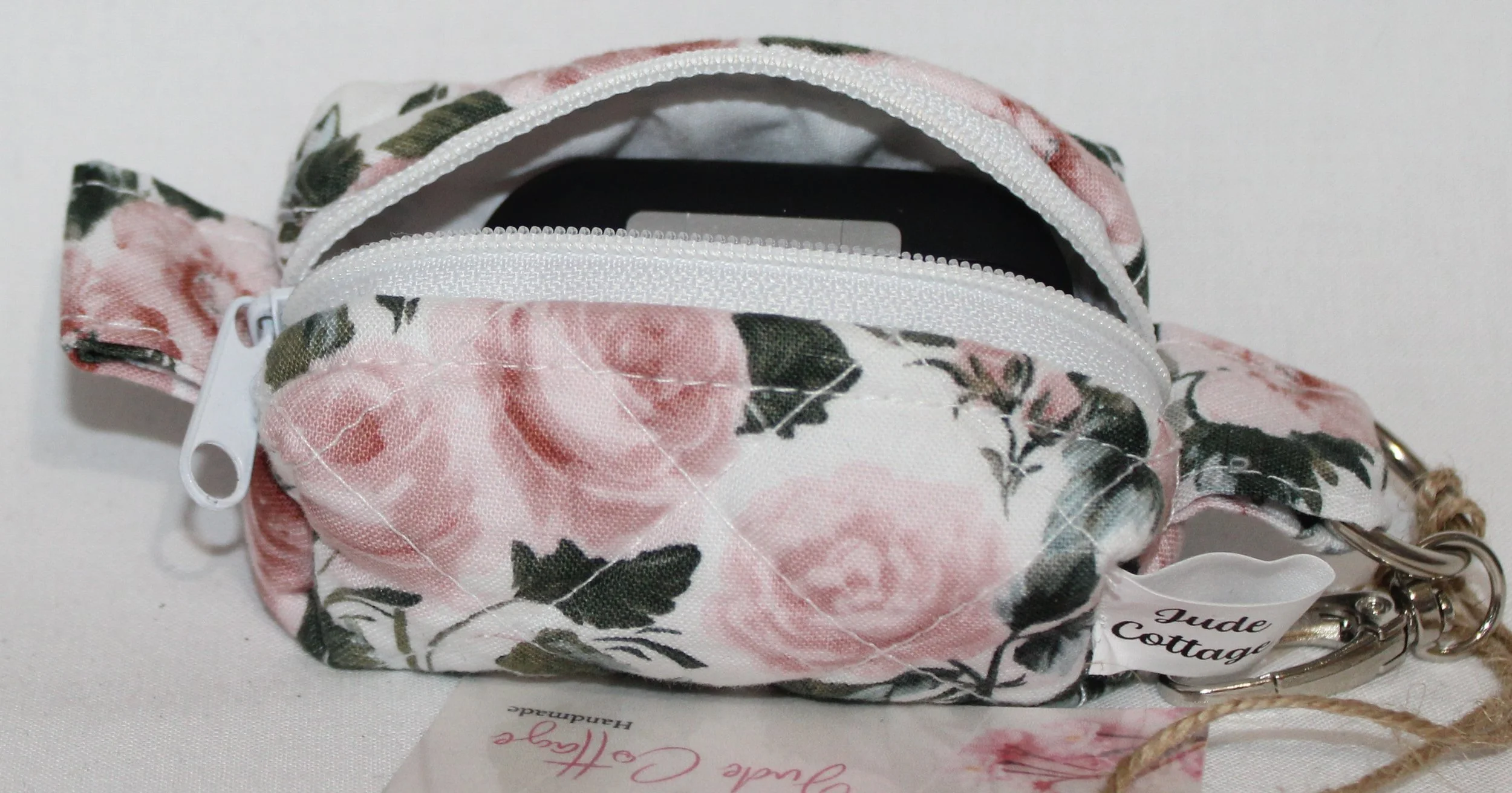 Open top view of the Rose Garden Bag Charm featuring white fabric with pink rose print shown with an Airpod Pro earbud case inserted for size reference.