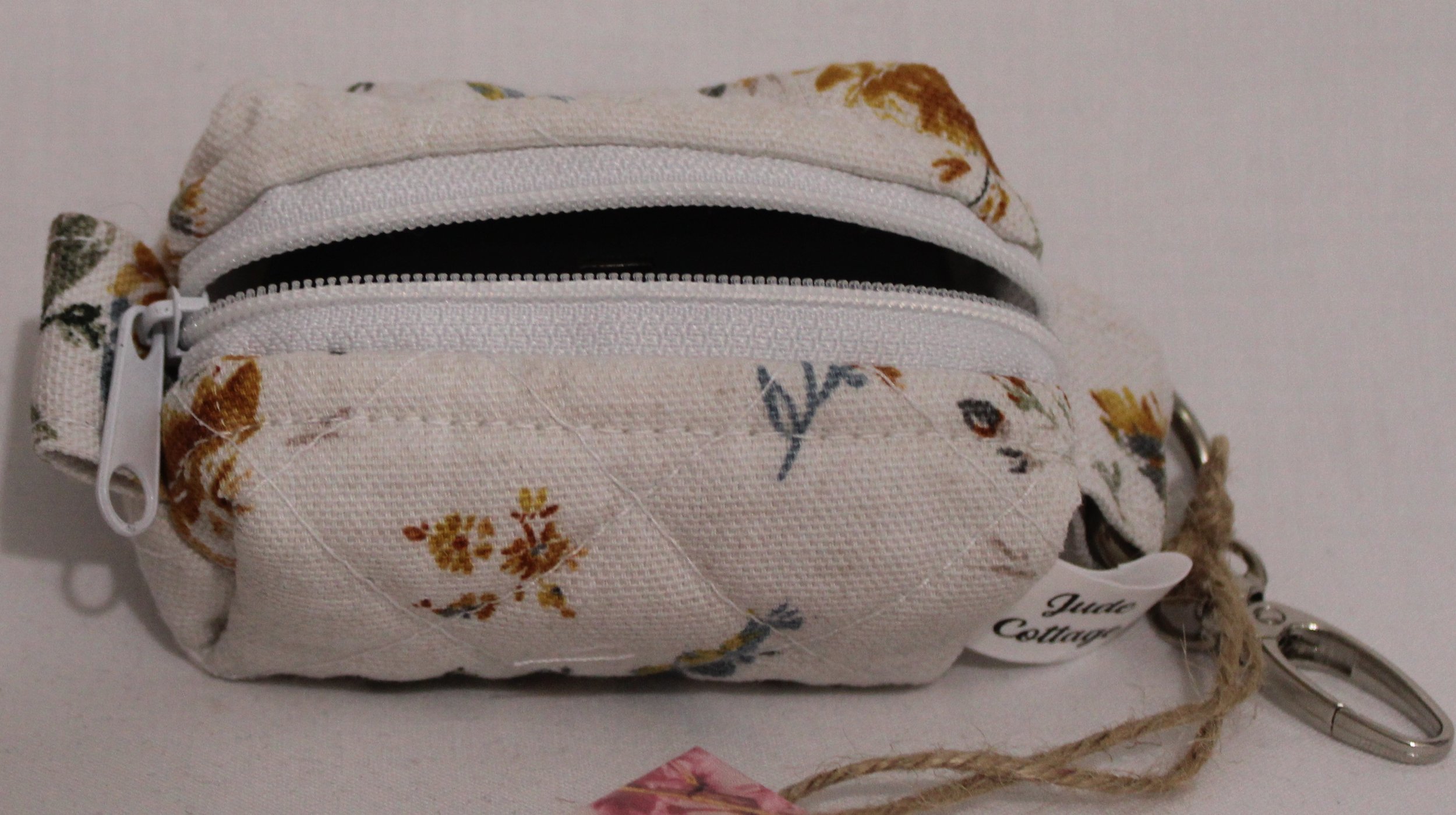 Top open view of the Dandelion Blue Bag Charm featuring assorted dandelions on an off white background and shown with a set of J Lab earbuds inserted for size reference.