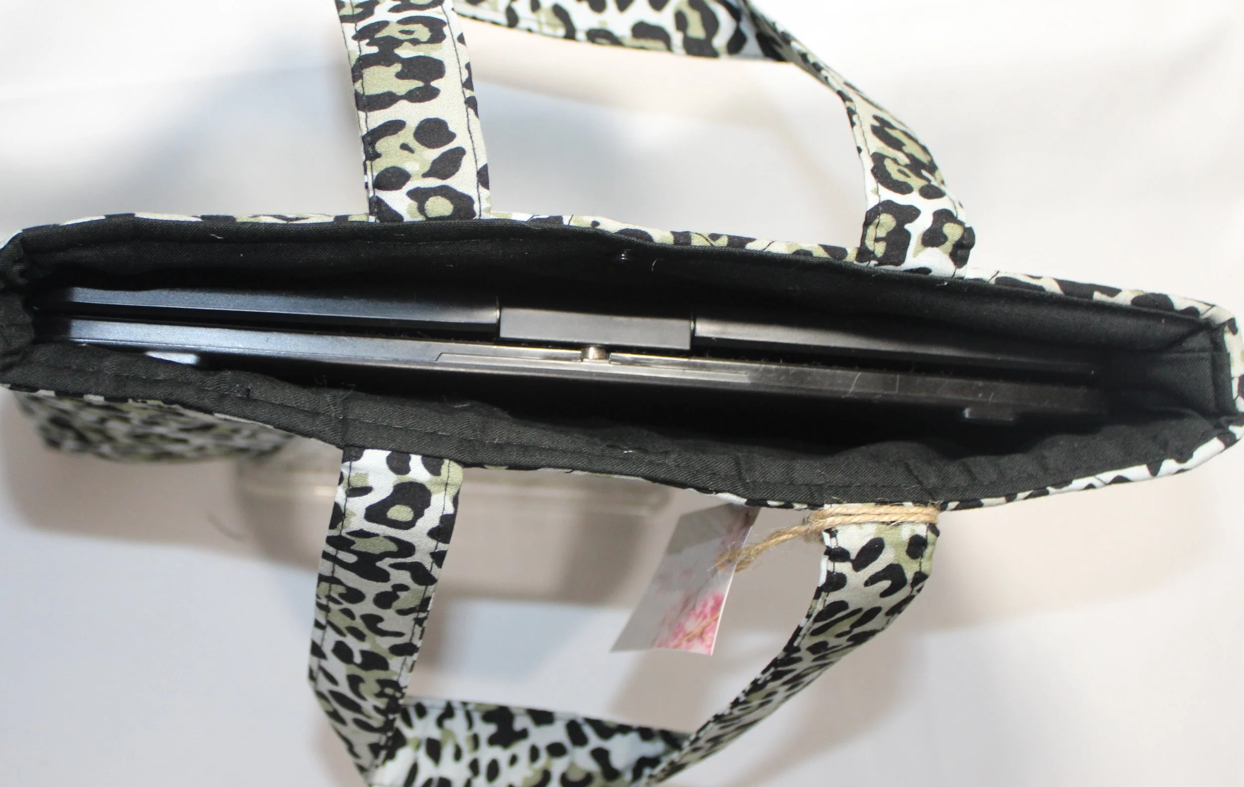 Top view of the Diana quilted animal‑print sleeve with snow leopard fabric, two carry handles, a snap closure, and a tablet inserted.