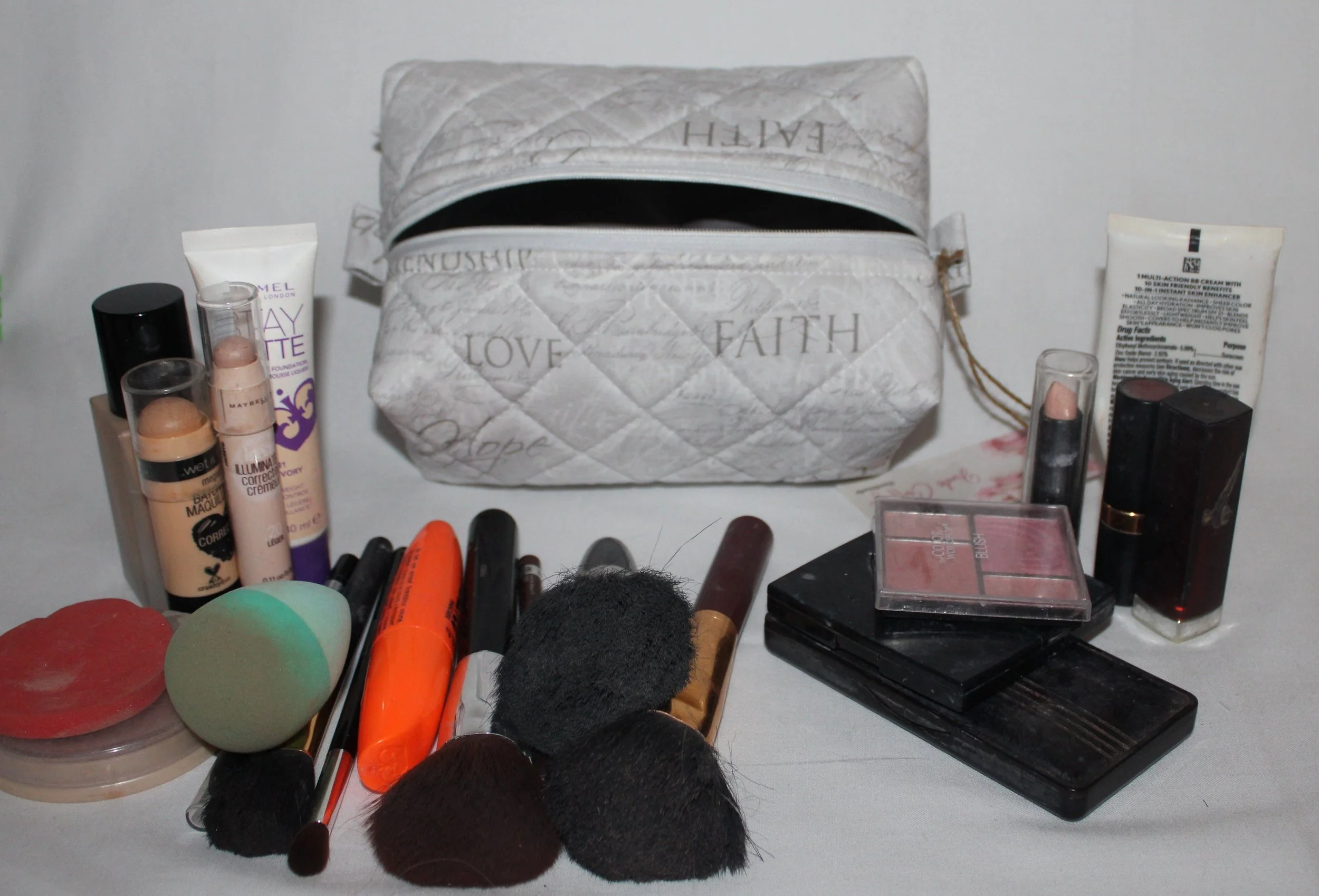 Faith Hope Love quilted cosmetic case in gray inspirational fabric shown with makeup and personal care items placed around it for scale.