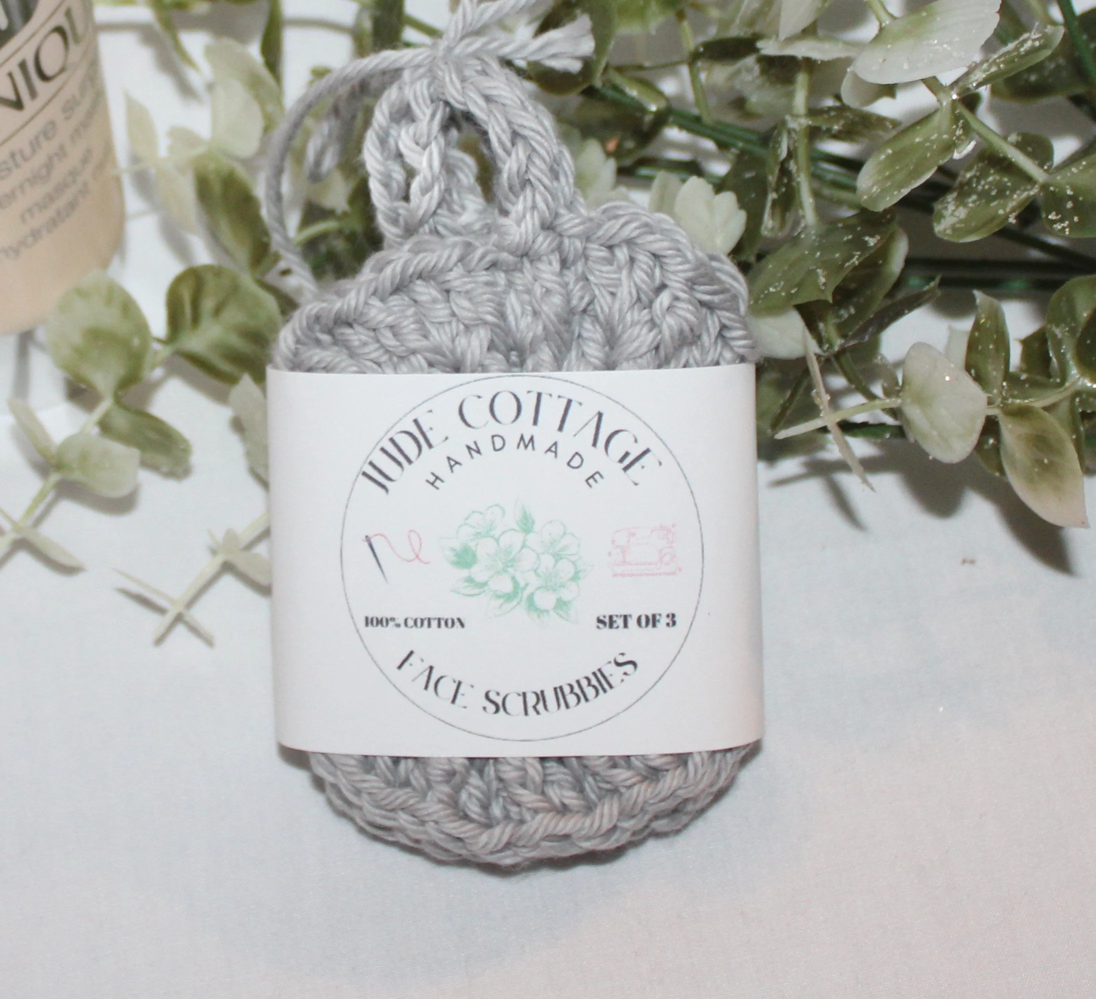 Close‑up of round crocheted silver facial scrubbies with a textured stitch pattern shown with label.