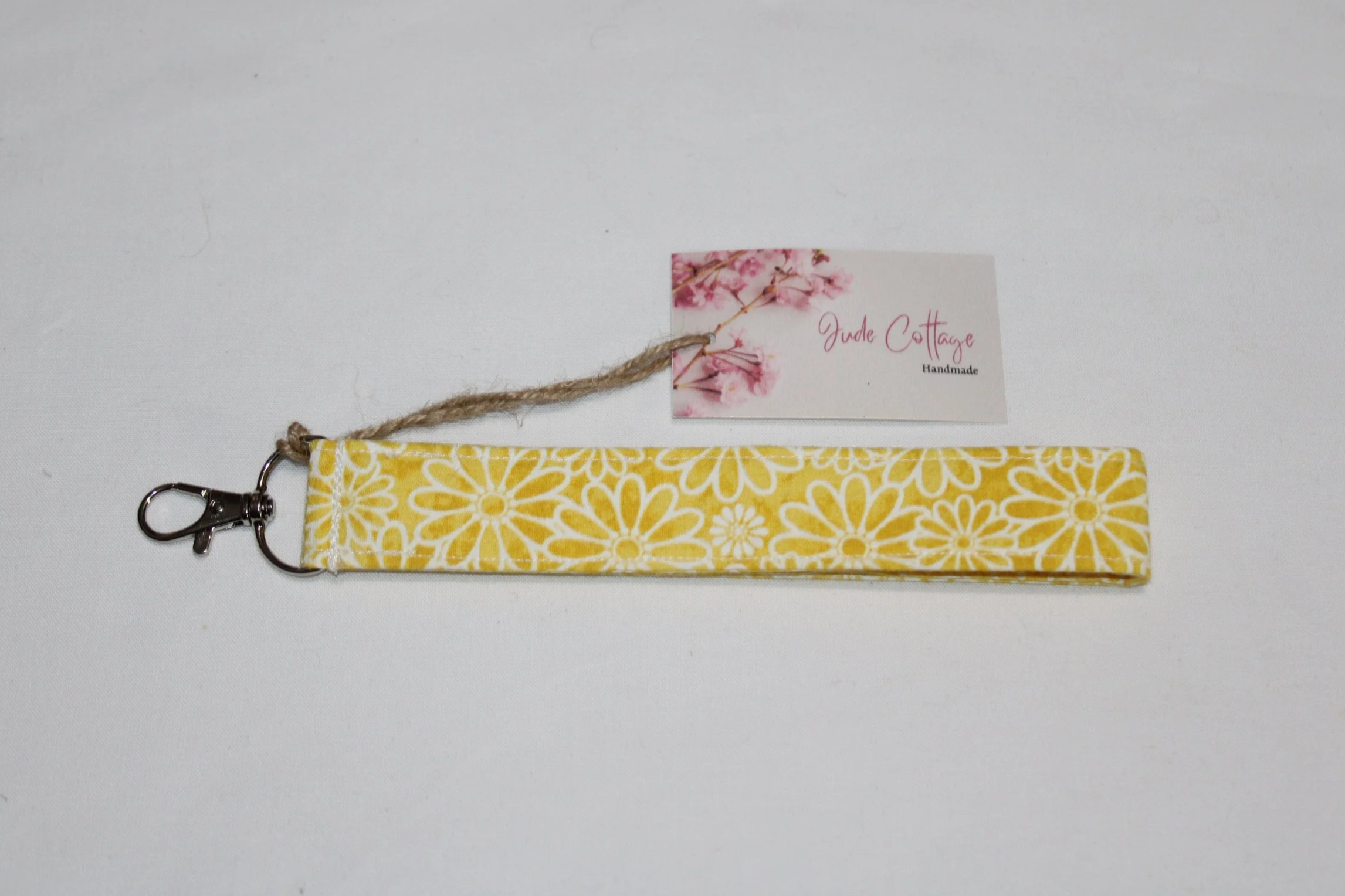 Gold Daisy Wristlet made from yellow fabric with a white daisy pattern, shown with an 8‑inch strap, metal clasp, and branded tag on a neutral background.