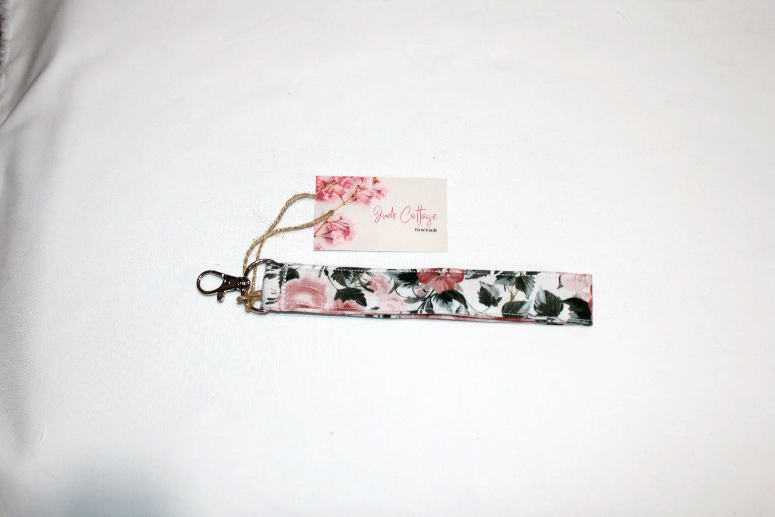 Close up view of the Rose Garden wristlet with a white background and pink rose fabric, showing the lobster clip to attach to wallet.