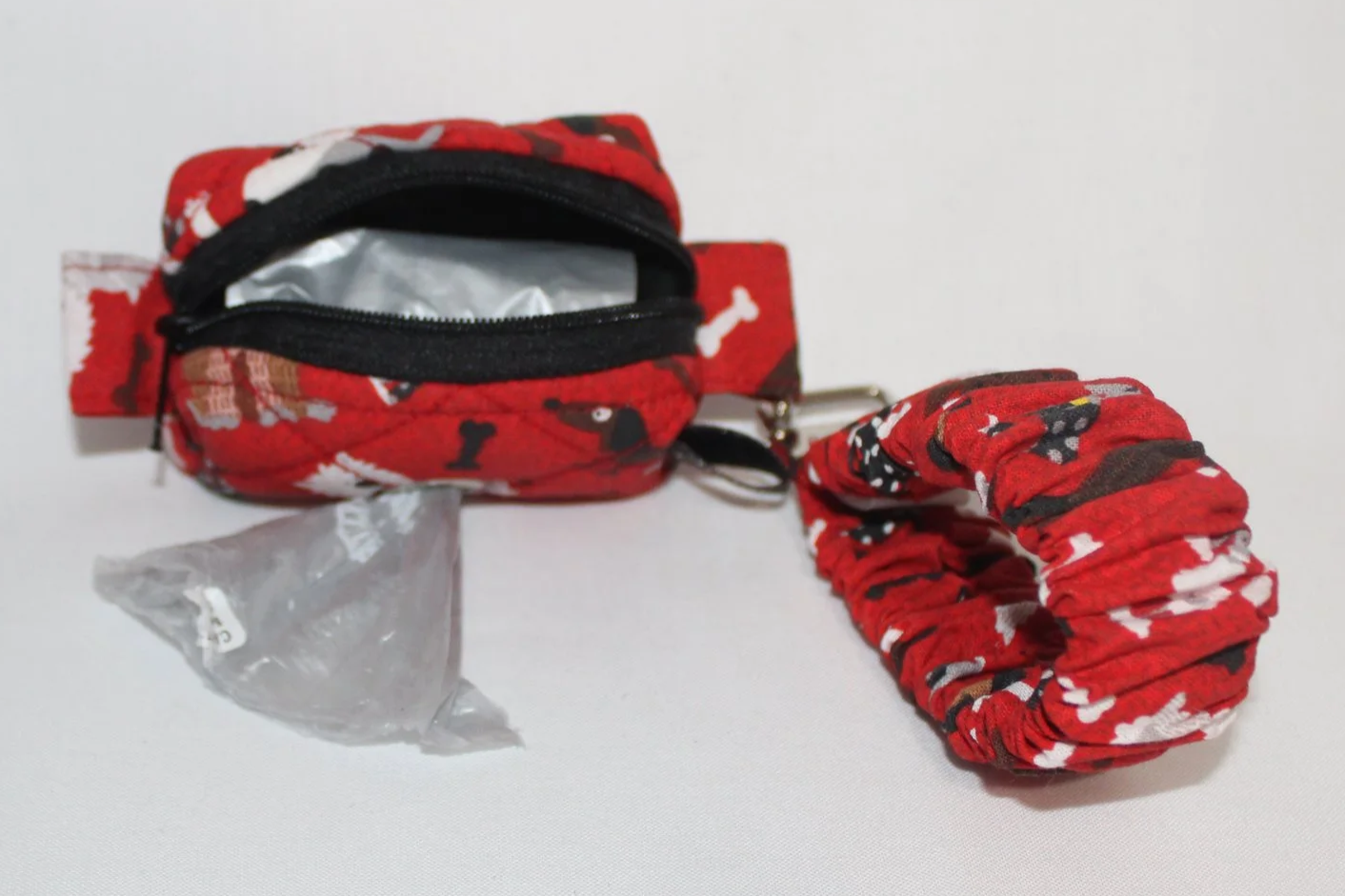 Open view of the Scarlet Dog puppy pouch in red fabric with dogs and bones pattern, with the matching scrunchie wristlet attached to the metal clip.