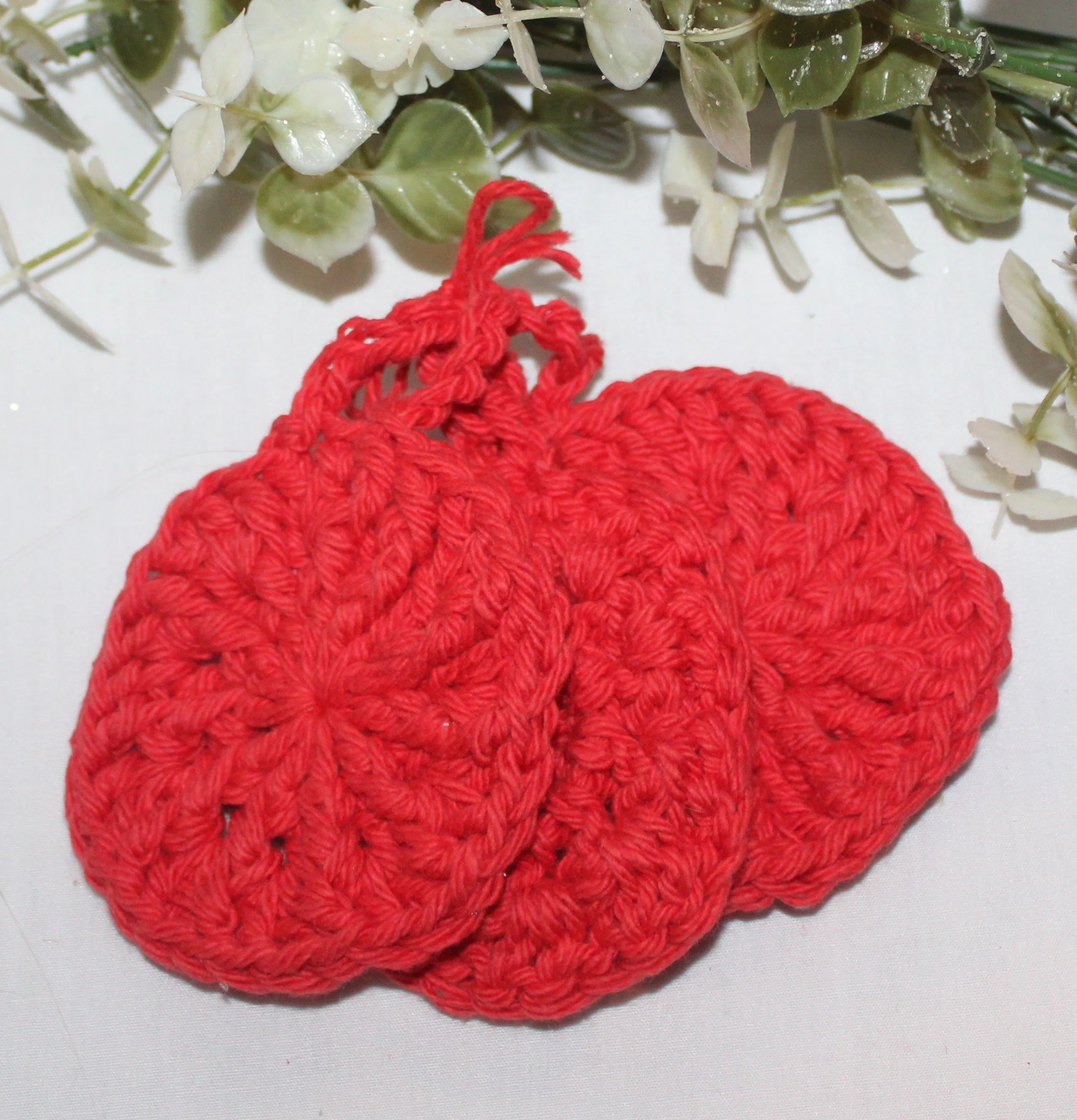 Close‑up of set of three round crocheted red facial scrubbies with a textured stitch pattern.